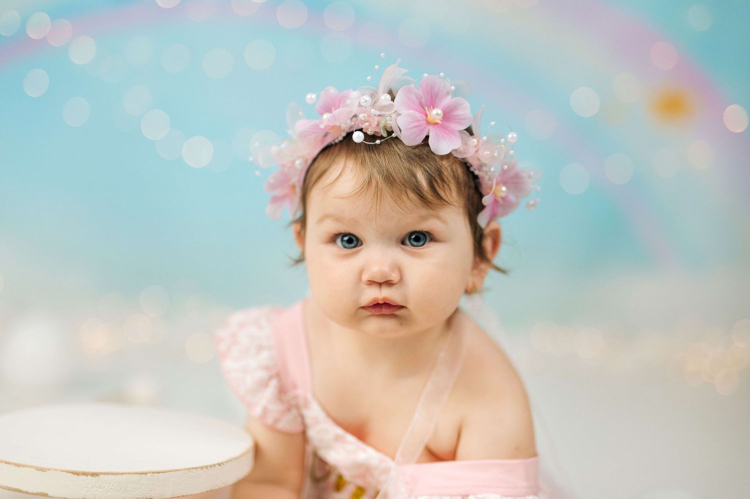 Baby girl in pink floral crown and ruffled outfit poses for first birthday cake smash photo session.