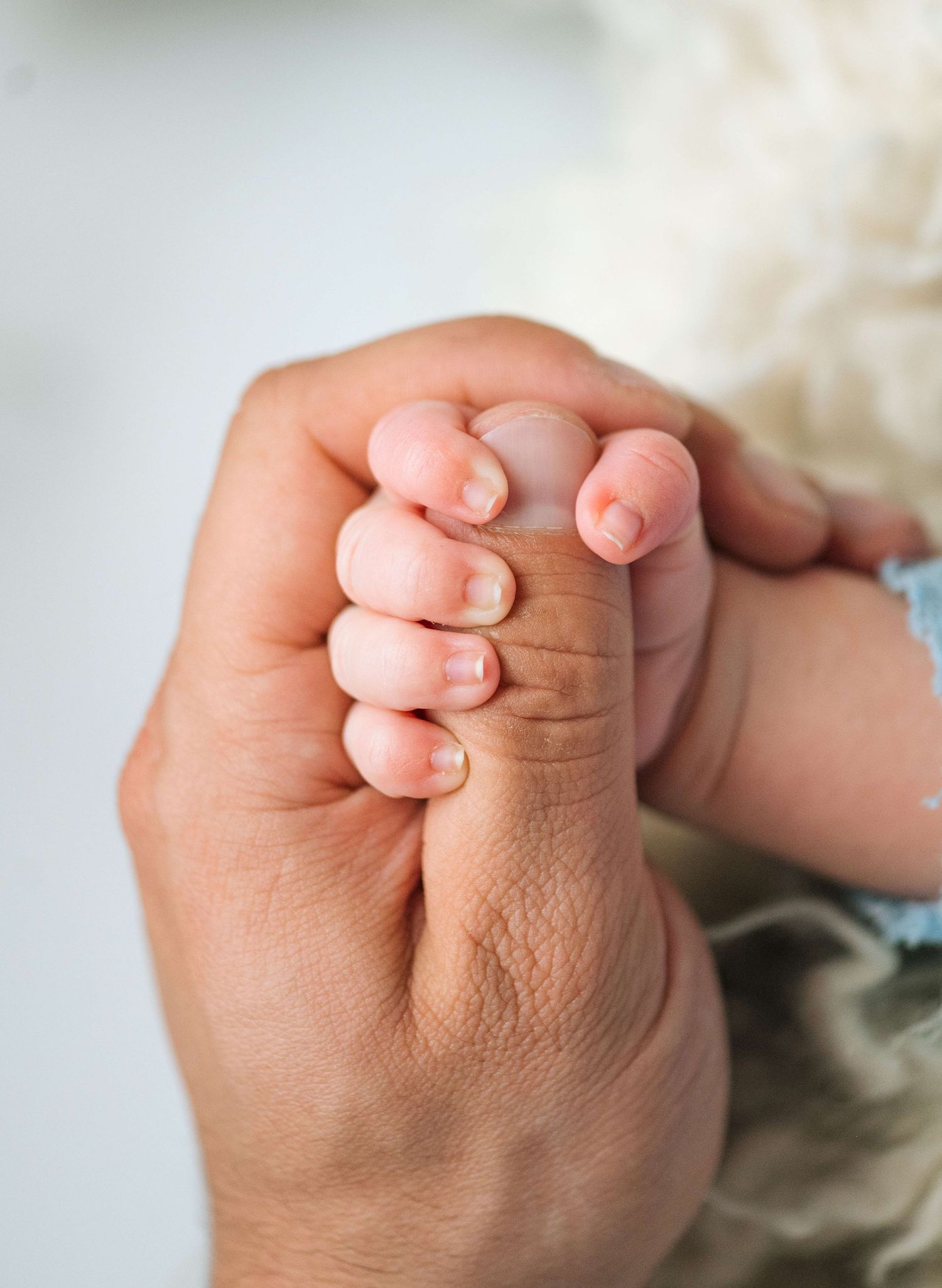 Close-up of a newborn baby's tiny hand gripping an adult's finger, symbolizing love and parental bond.