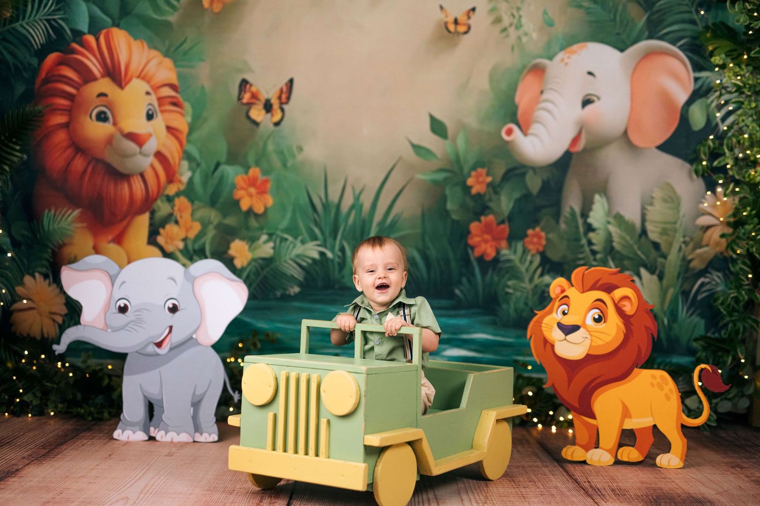Baby smiling in toy jeep surrounded by cartoon jungle animals with lion and elephant cutouts on wooden floor.