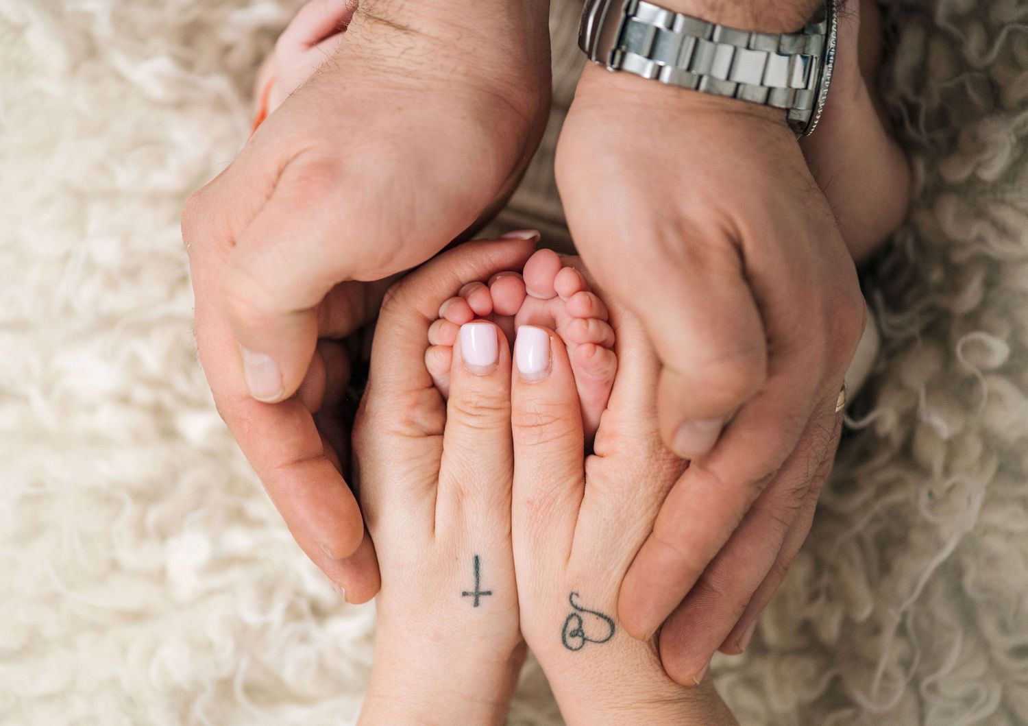 Parents and newborn baby hands together, showing small tattoos on mother's wrist, a tender family moment.