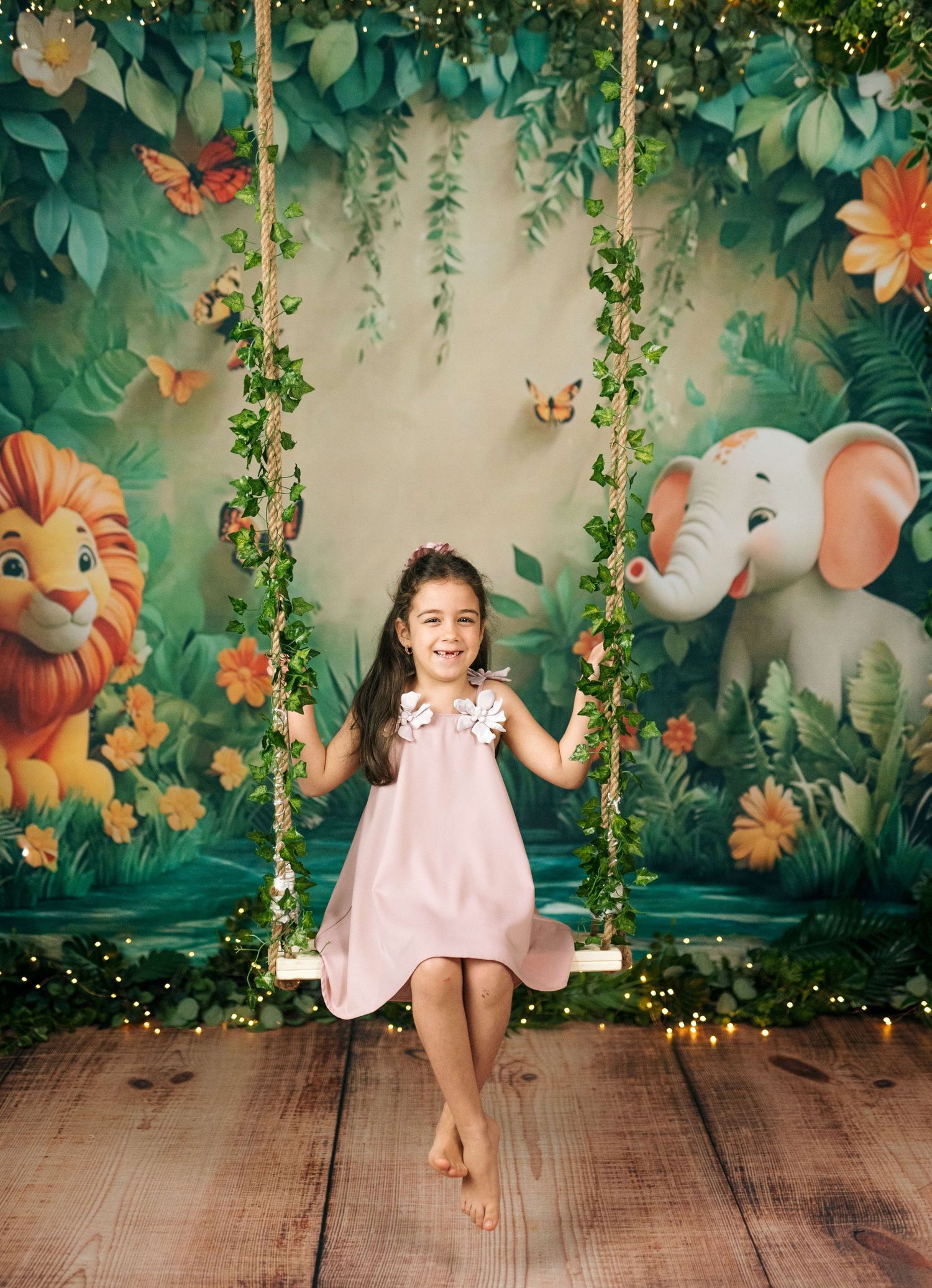 A smiling girl in a pink dress sits on a vine-covered swing against a jungle backdrop with cartoon lion and elephant.