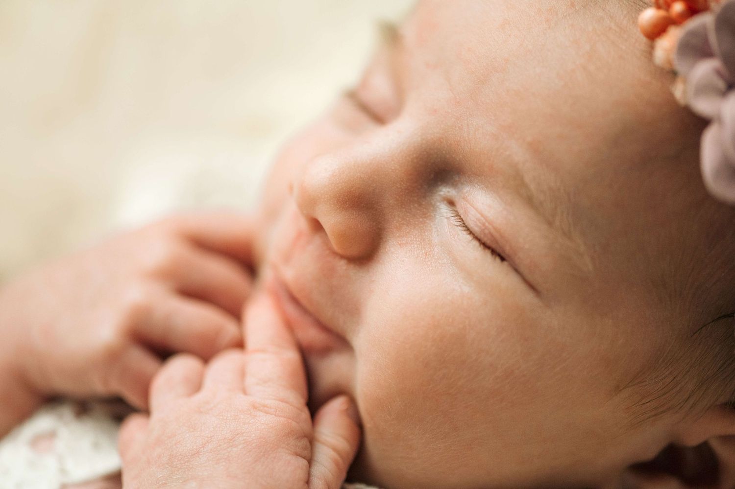 Peaceful sleeping newborn baby with flower headband, eyes closed, tiny fingers near face, soft warm tones.