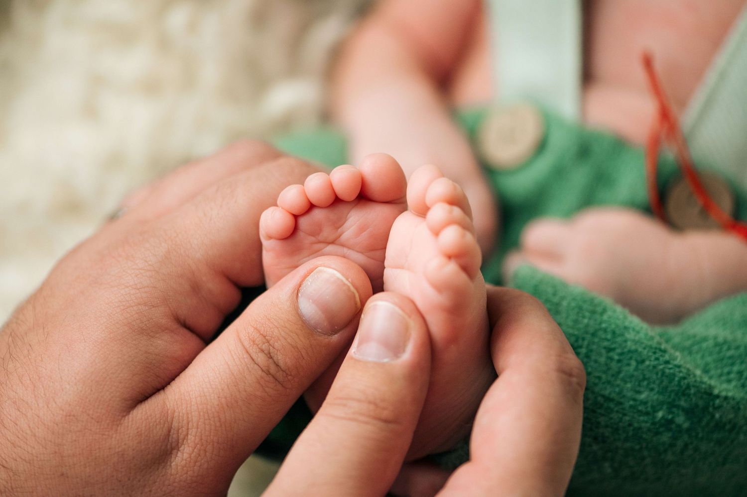 Close-up of adult hands gently cradling tiny newborn baby feet wrapped in a green blanket.