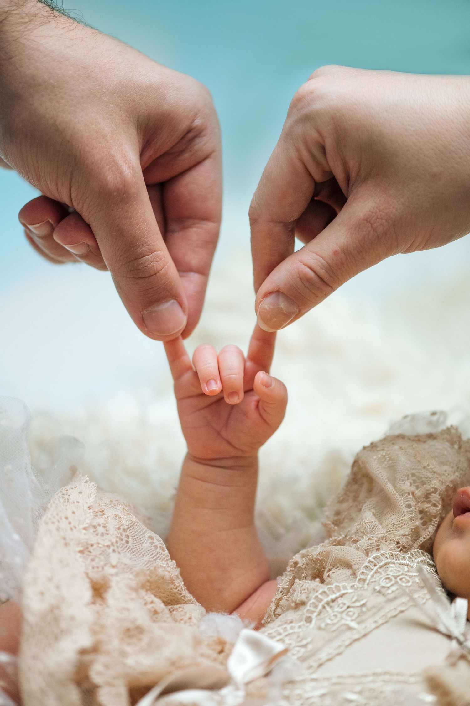 Newborn baby grasping parents fingers, close-up of tiny infant hand holding adult fingers in lace outfit.