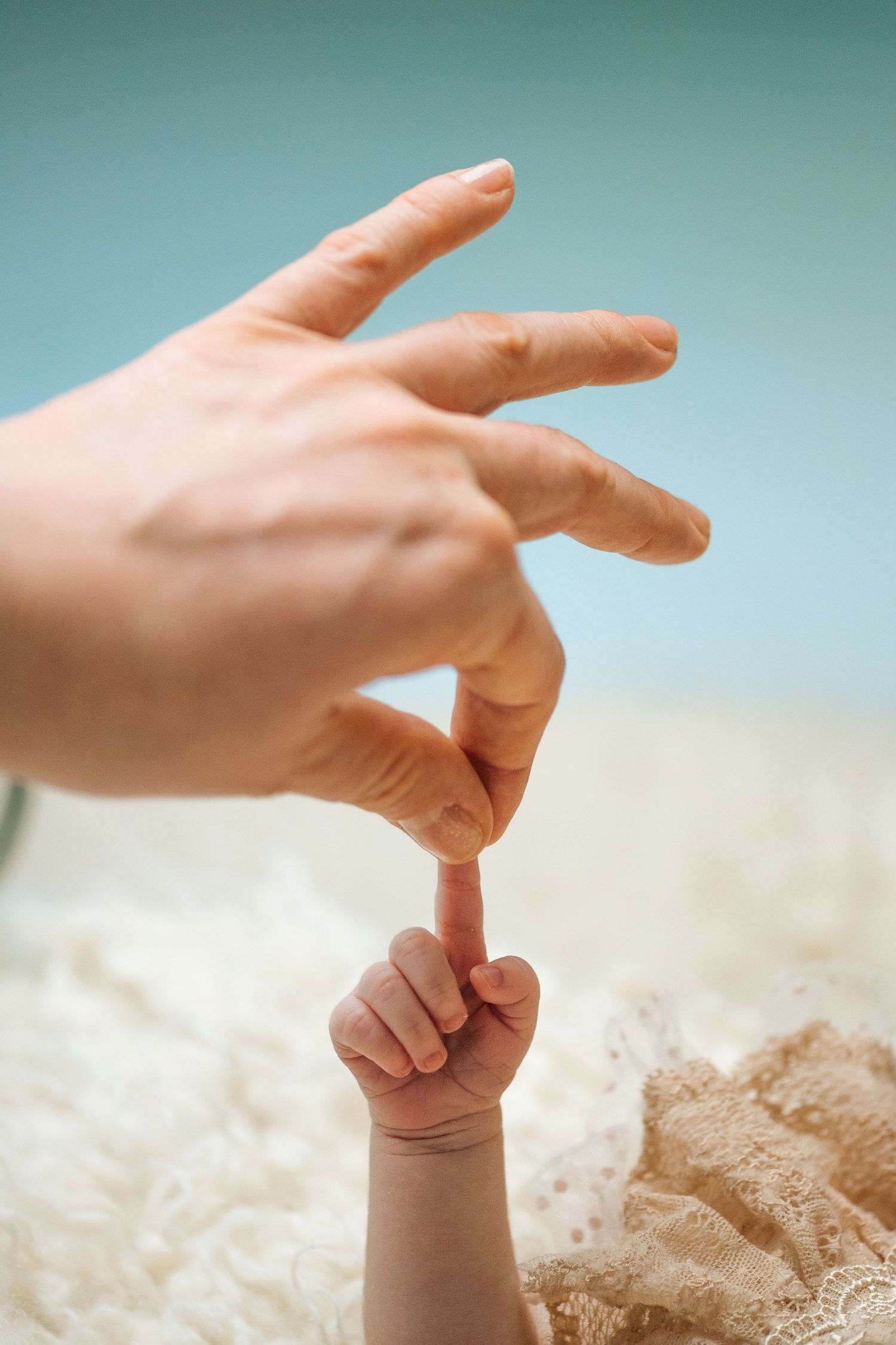 A tiny baby finger touching an adult's finger against a soft blue background, symbolizing family bond.