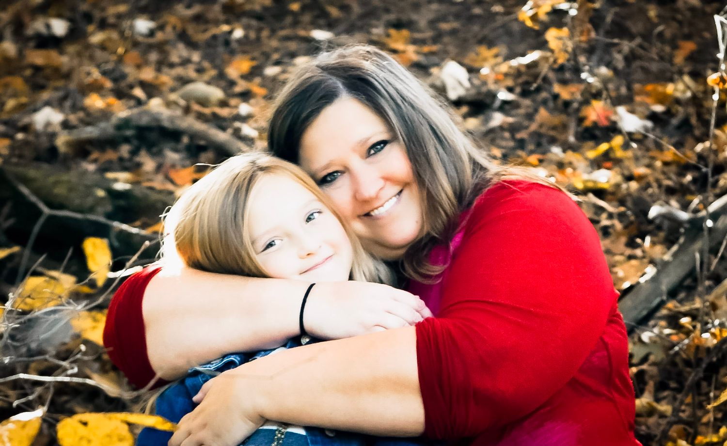 A smiling mother and young child share a warm hug outdoors among autumn leaves in a heartfelt fall portrait.
