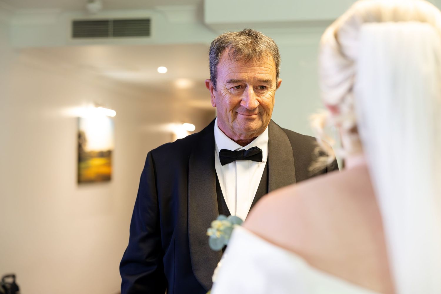 An emotional father gazing at his daughter the bride during a wedding ceremony indoors.