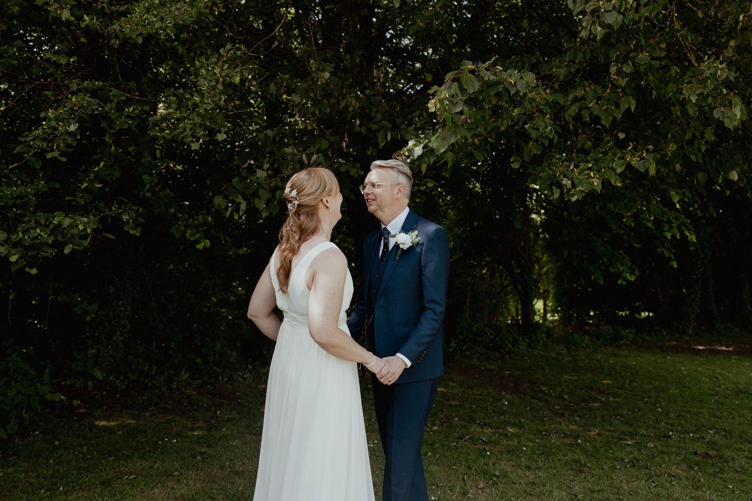 Bride and groom walk hand in hand through a lush green garden on their wedding day.