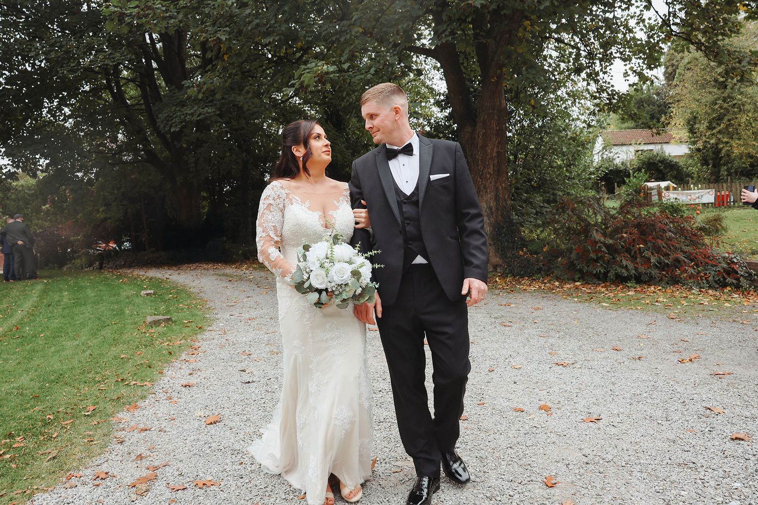 Bride and groom walking together on a gravel path, smiling at each other, bride holding white bouquet. South Wales wedding photography