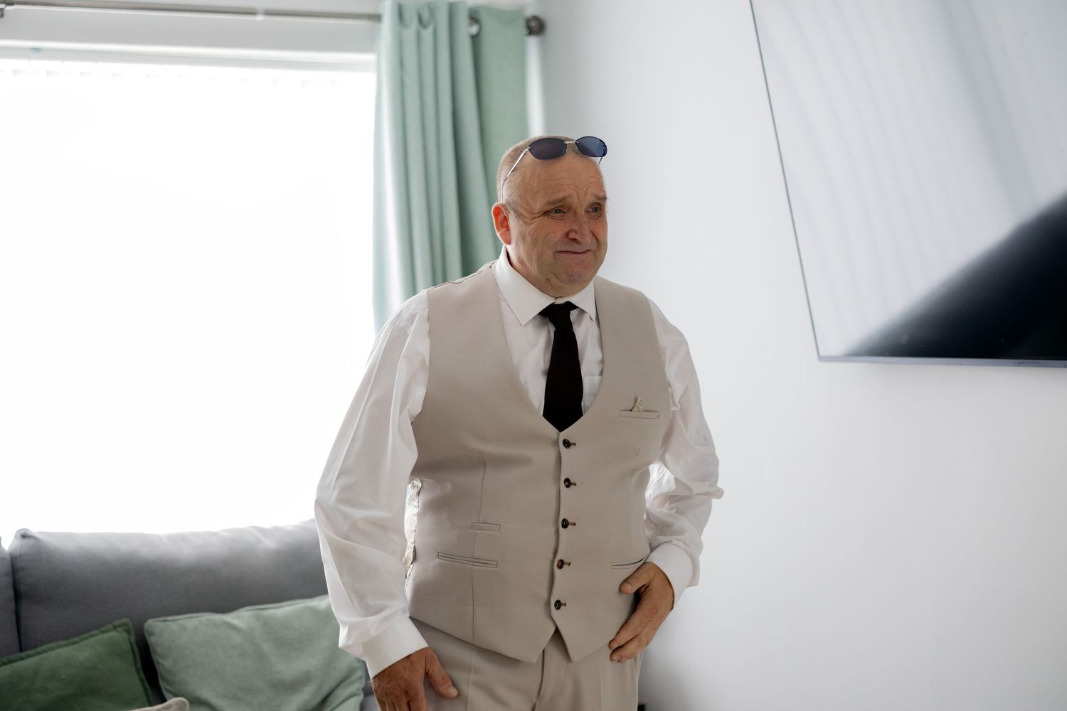 Dapper man in white shirt, grey vest and black tie standing in bright room.