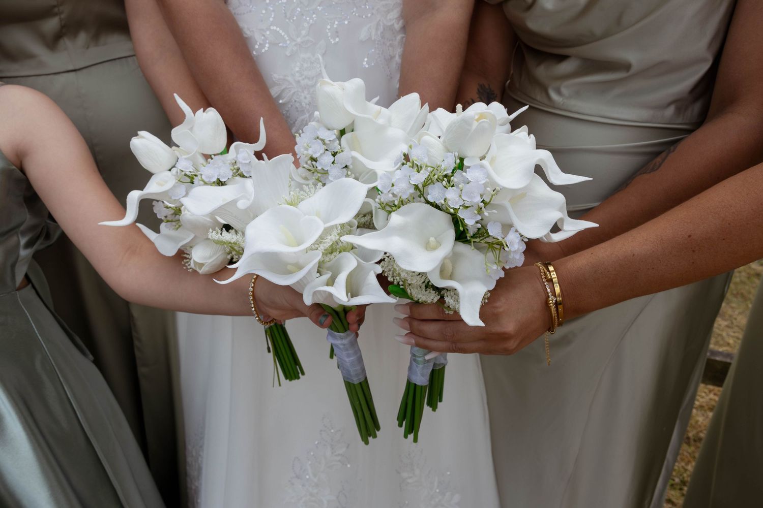 Bridesmaids and bride holding elegant white calla lily bouquets at a wedding ceremony.