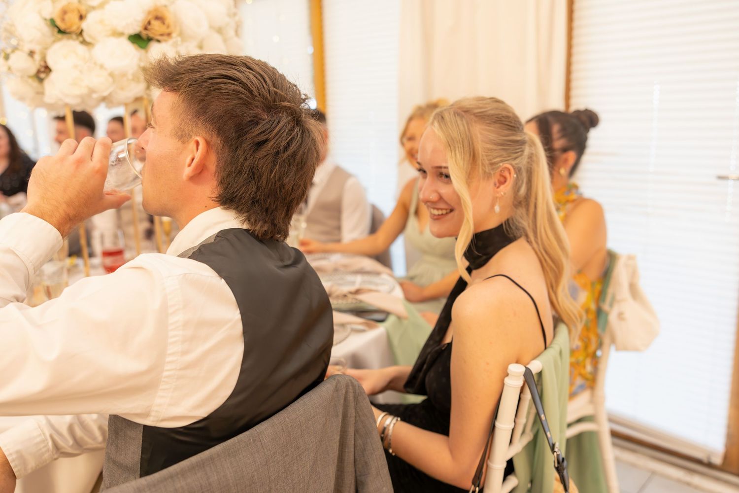 Young wedding guests smiling and chatting at elegantly decorated white wedding reception table.