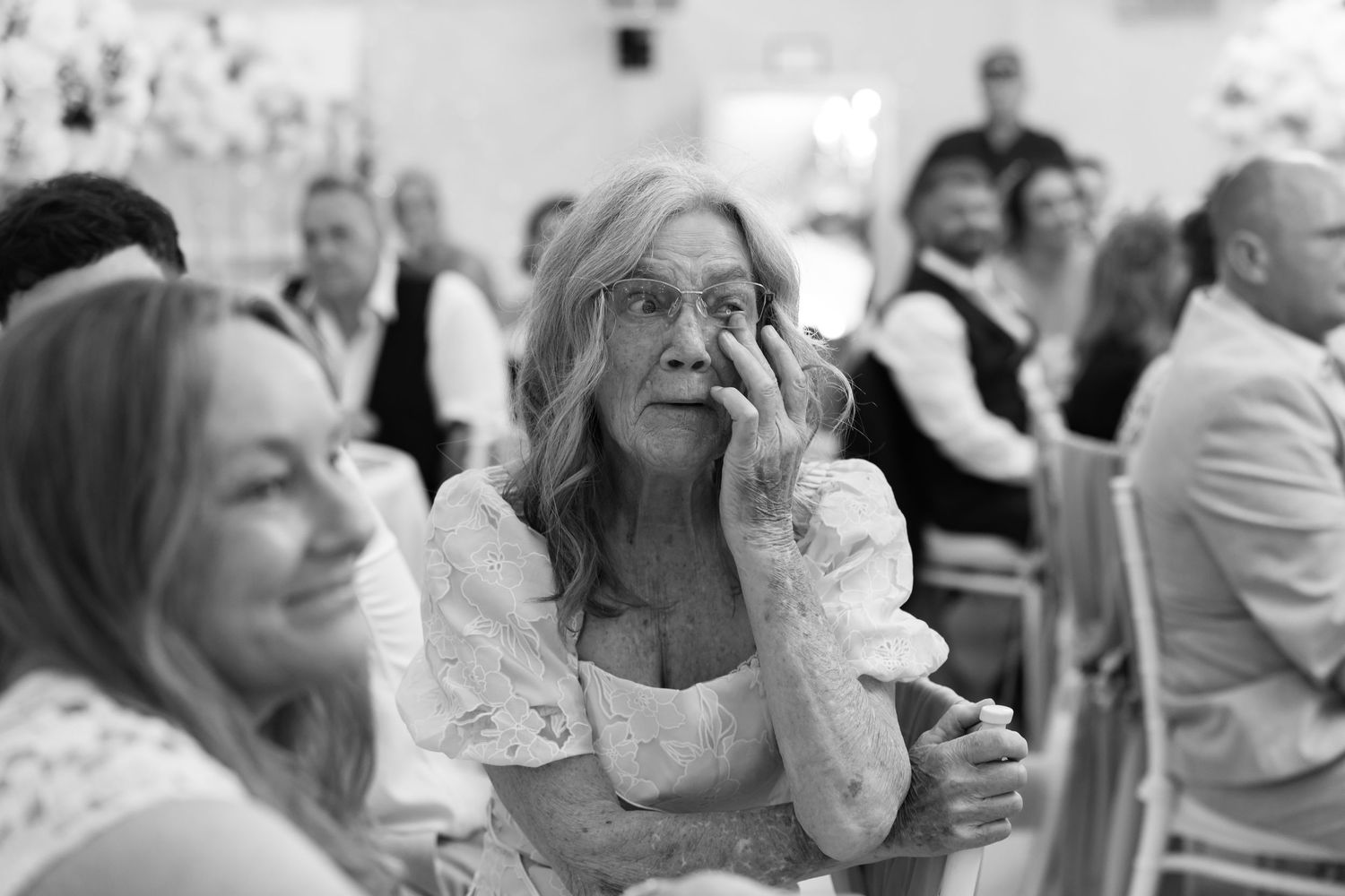 Elderly woman wiping tears at a wedding reception, captured in black and white.