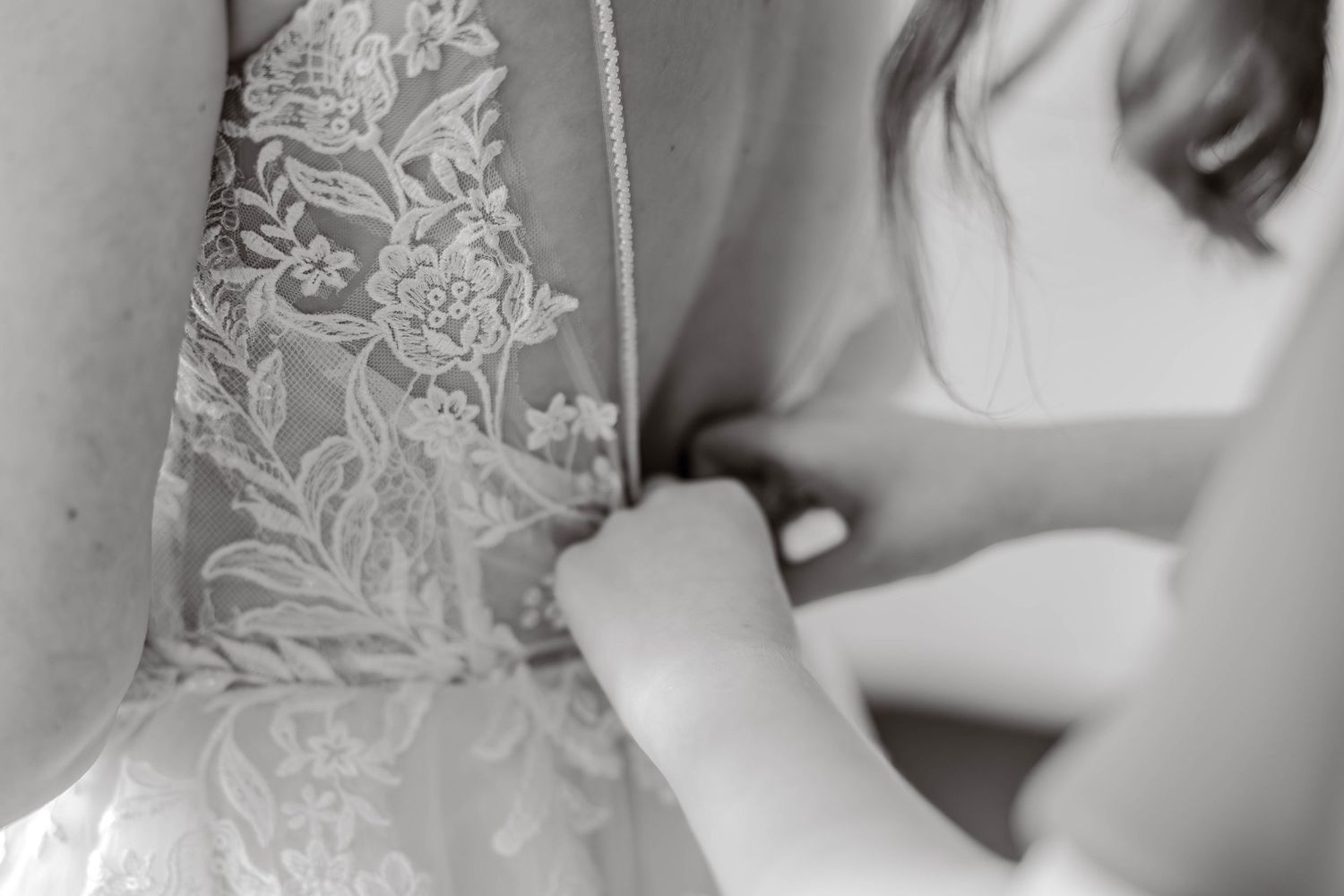 Black and white close-up of intricate floral lace detailing on a bridal gown being fastened.
