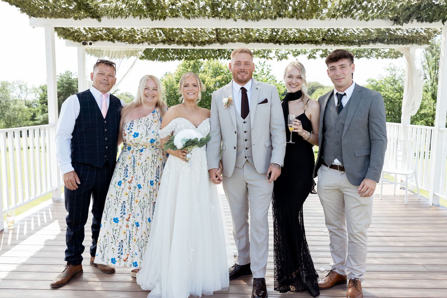 Wedding party group photo featuring bride in white gown with guests in floral, mint and black dresses.