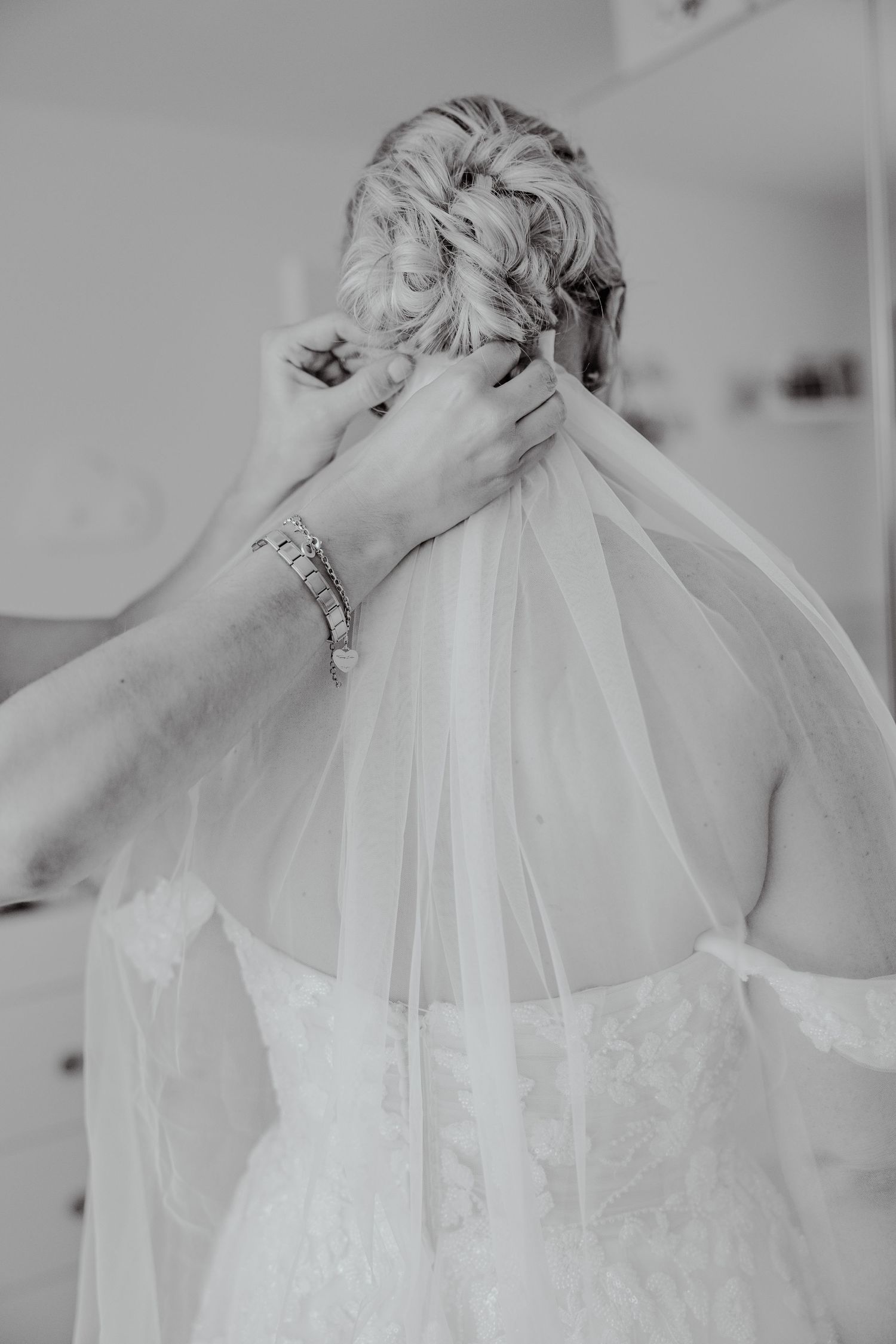 Close-up black and white shot of hands carefully attaching a veil to the brides upswept hair.