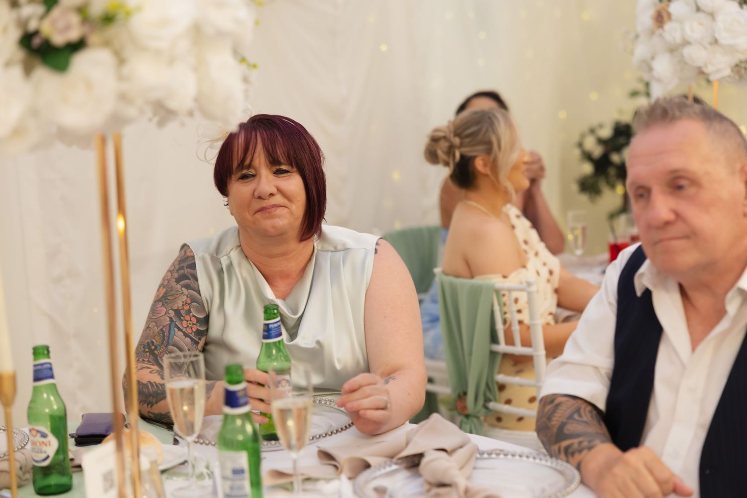 Wedding guest with tattoos smiling at decorated reception table with champagne.