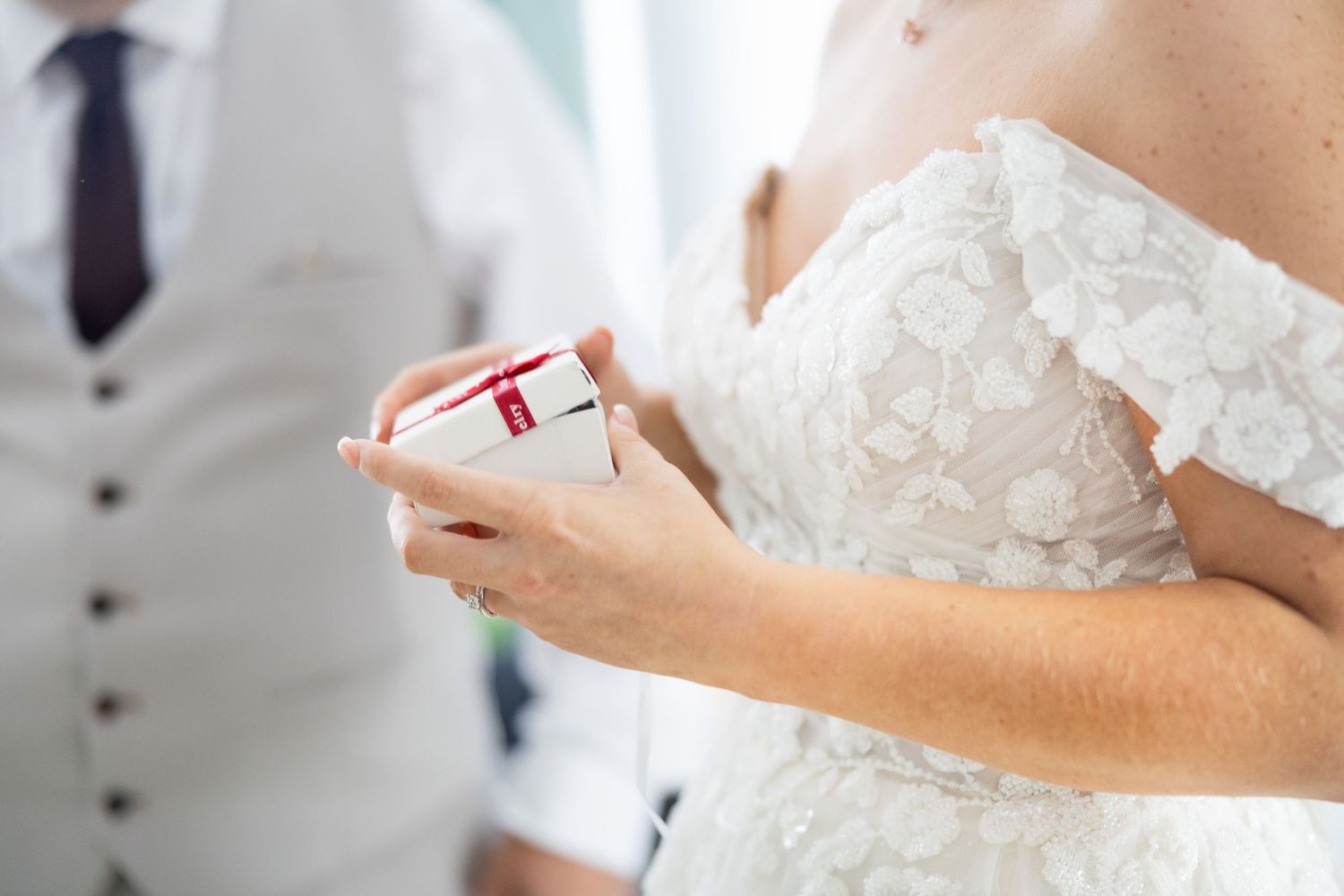 Close-up of bride in lace dress holding small red gift box at wedding.