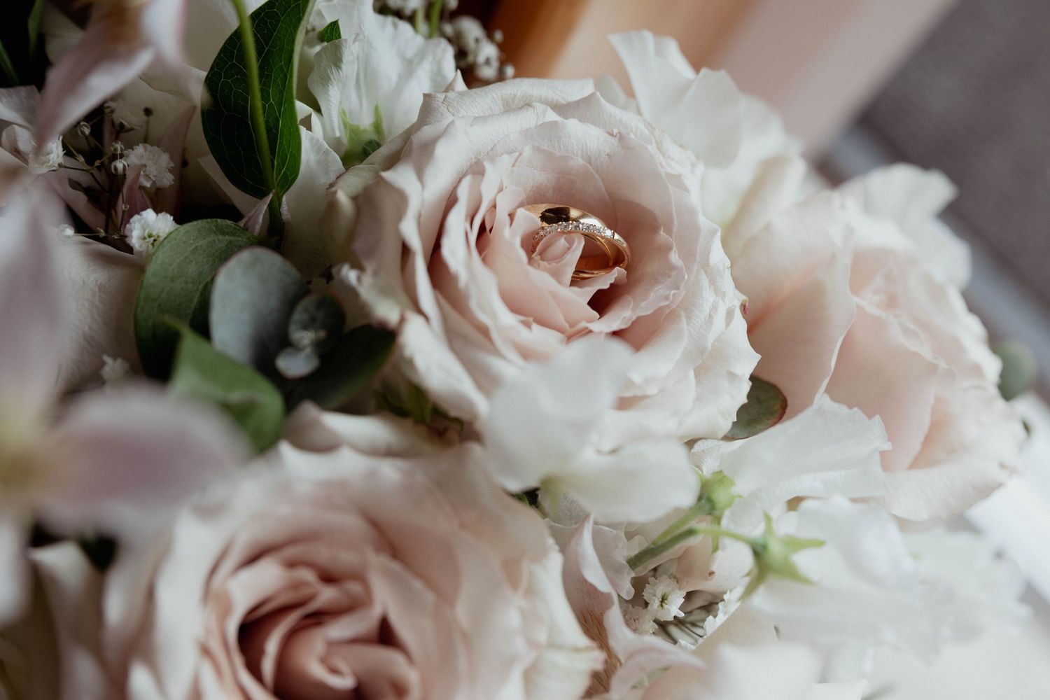 Close-up of elegant wedding bouquet featuring blush roses with gold rings nestled in blooms.