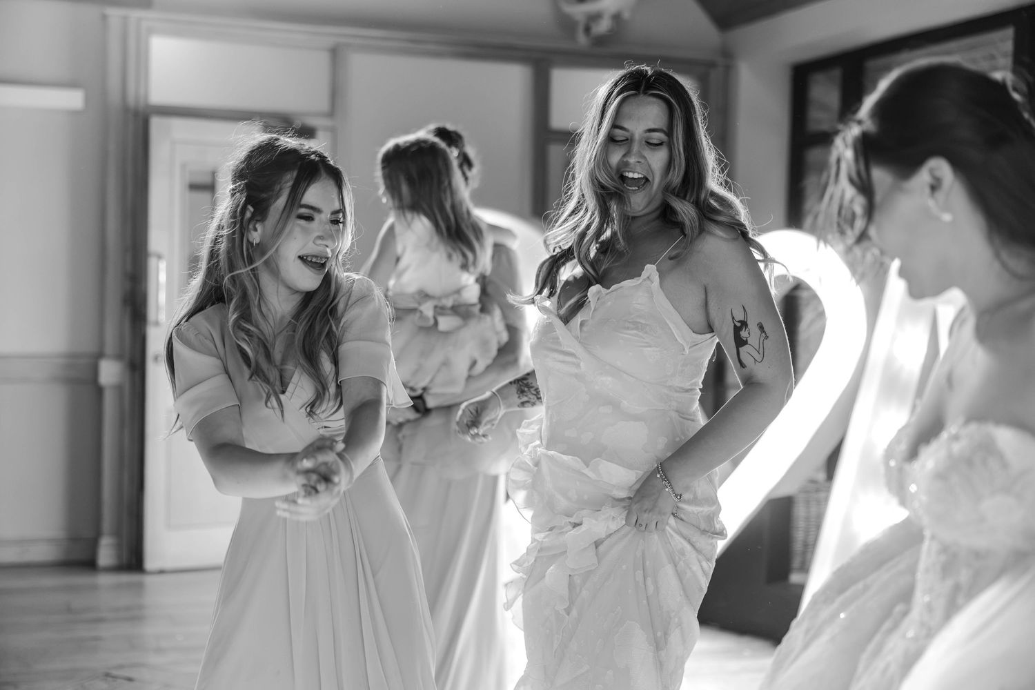 Black and white photo of bride laughing and dancing with bridesmaids at wedding reception.