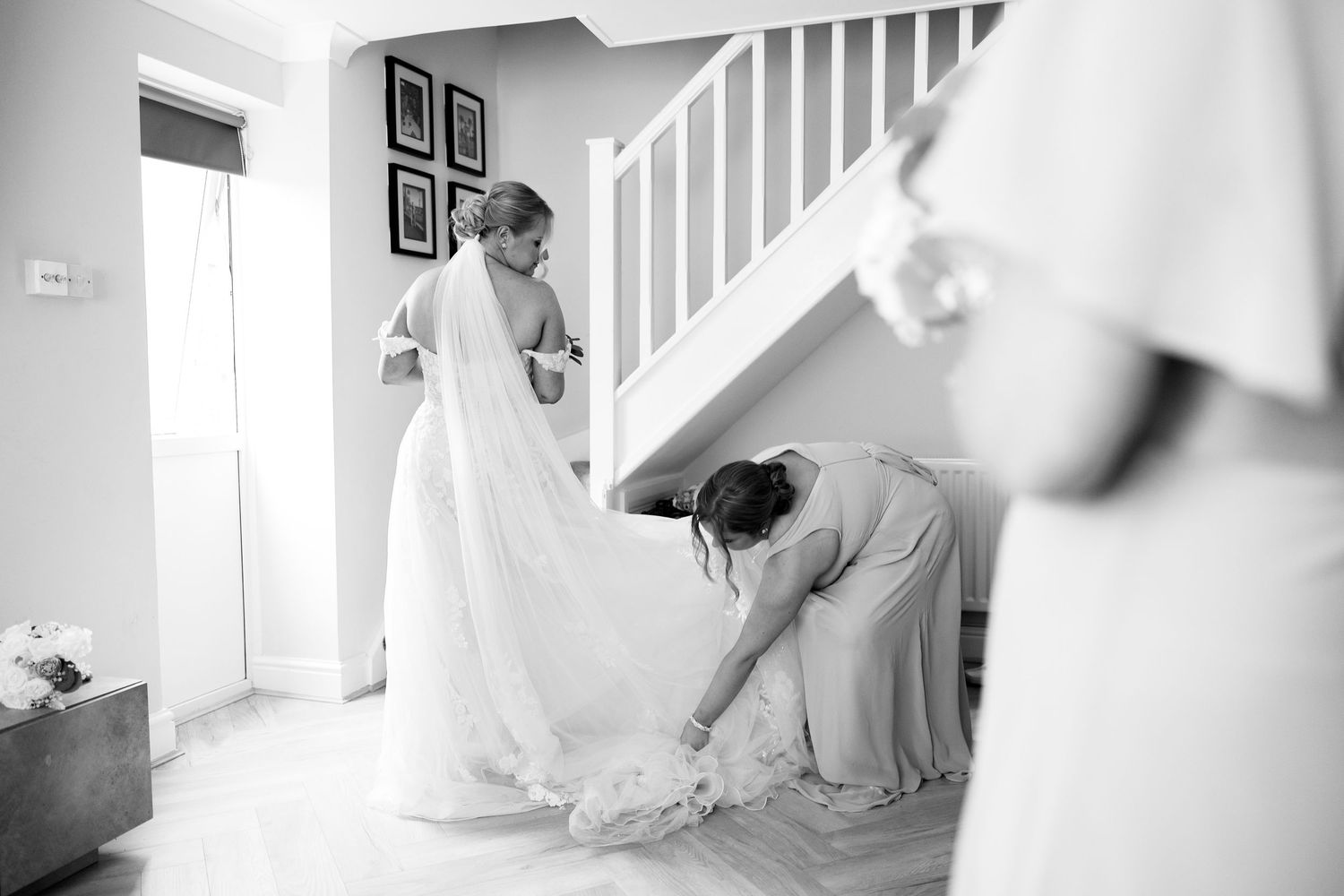 Black and white image of a bridesmaid arranging the brides flowing wedding dress train by the stairs.