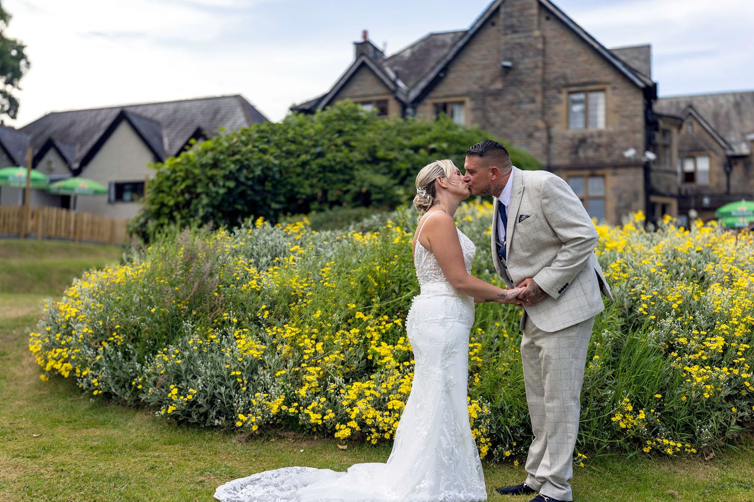 A bride and groom share a romantic kiss in front of vibrant yellow flowers at an outdoor wedding venue. maes manor hotel wedding photography