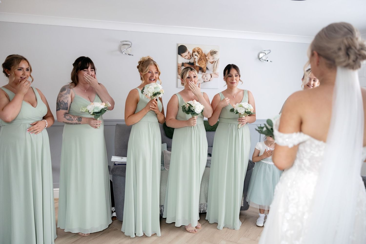 Bridesmaids in sage green dresses react emotionally seeing bride in wedding gown.