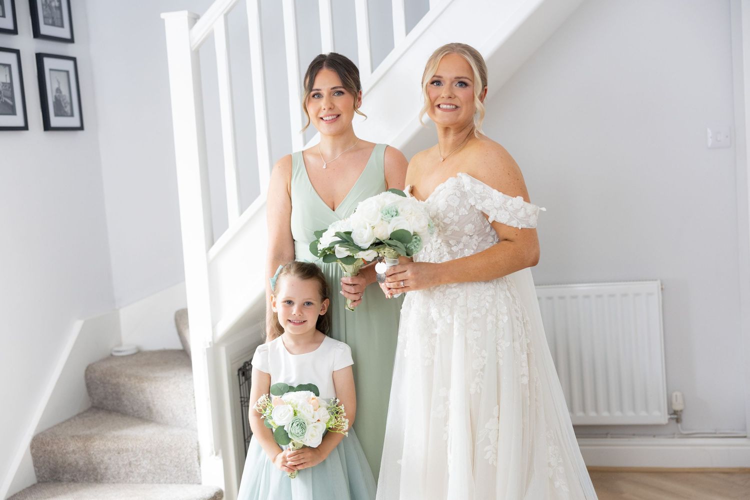 Bride with bridesmaid and flower girl in sage green dresses holding white bouquets.