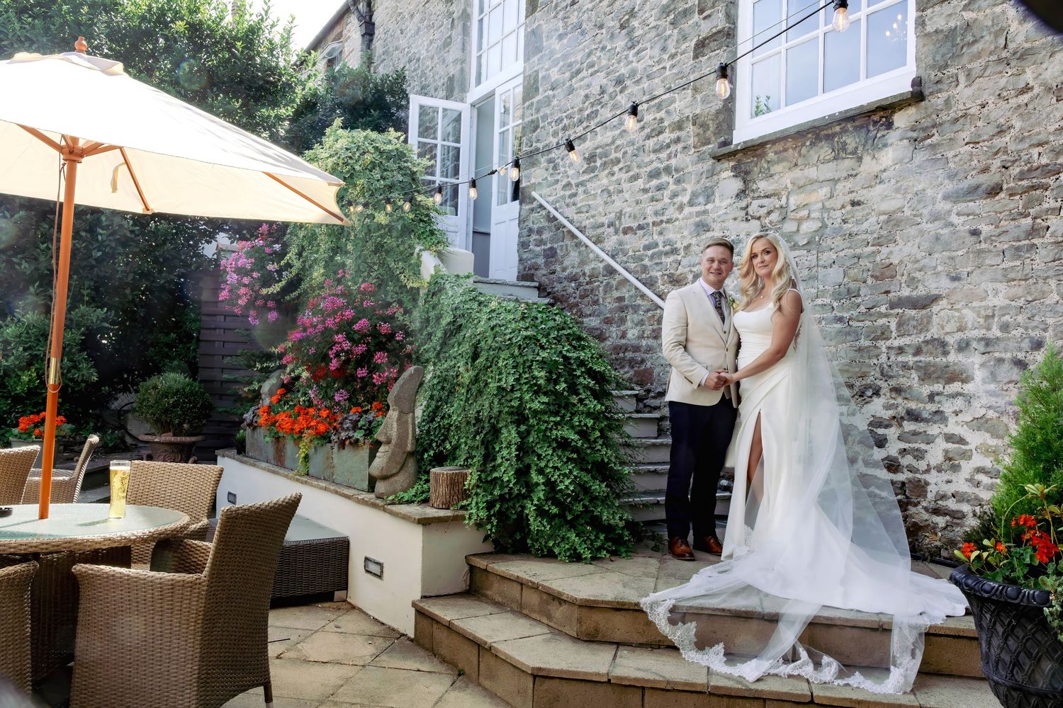 Newlywed couple posing together in romantic stone courtyard garden after their wedding ceremony.