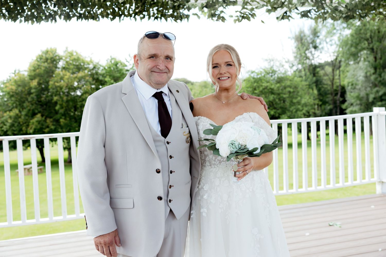 Bride and groom smiling together on wooden deck at outdoor wedding venue on sunny day.