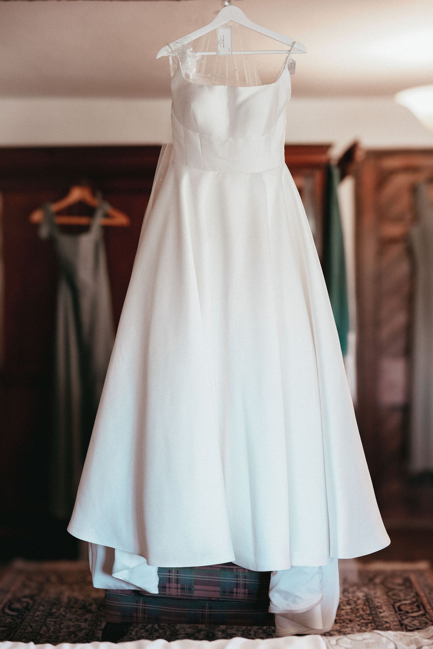 Elegant strapless white ball gown wedding dress hanging on a wooden wardrobe in a softly lit room.