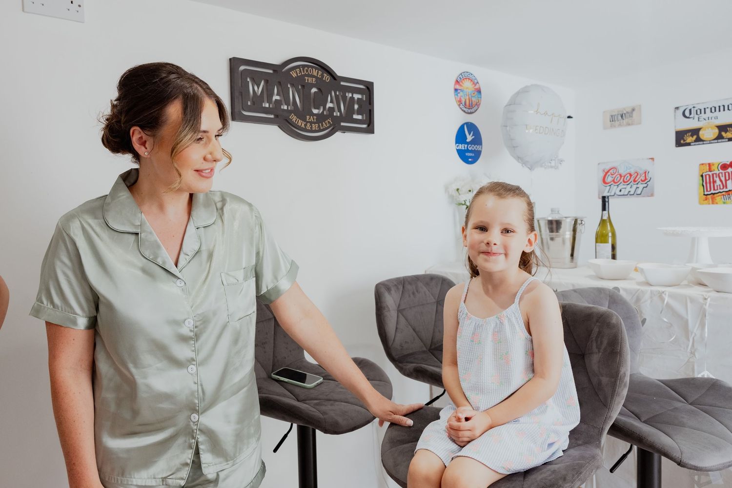 Bridesmaid in sage green satin pyjamas smiling with a young flower girl in a white dress.