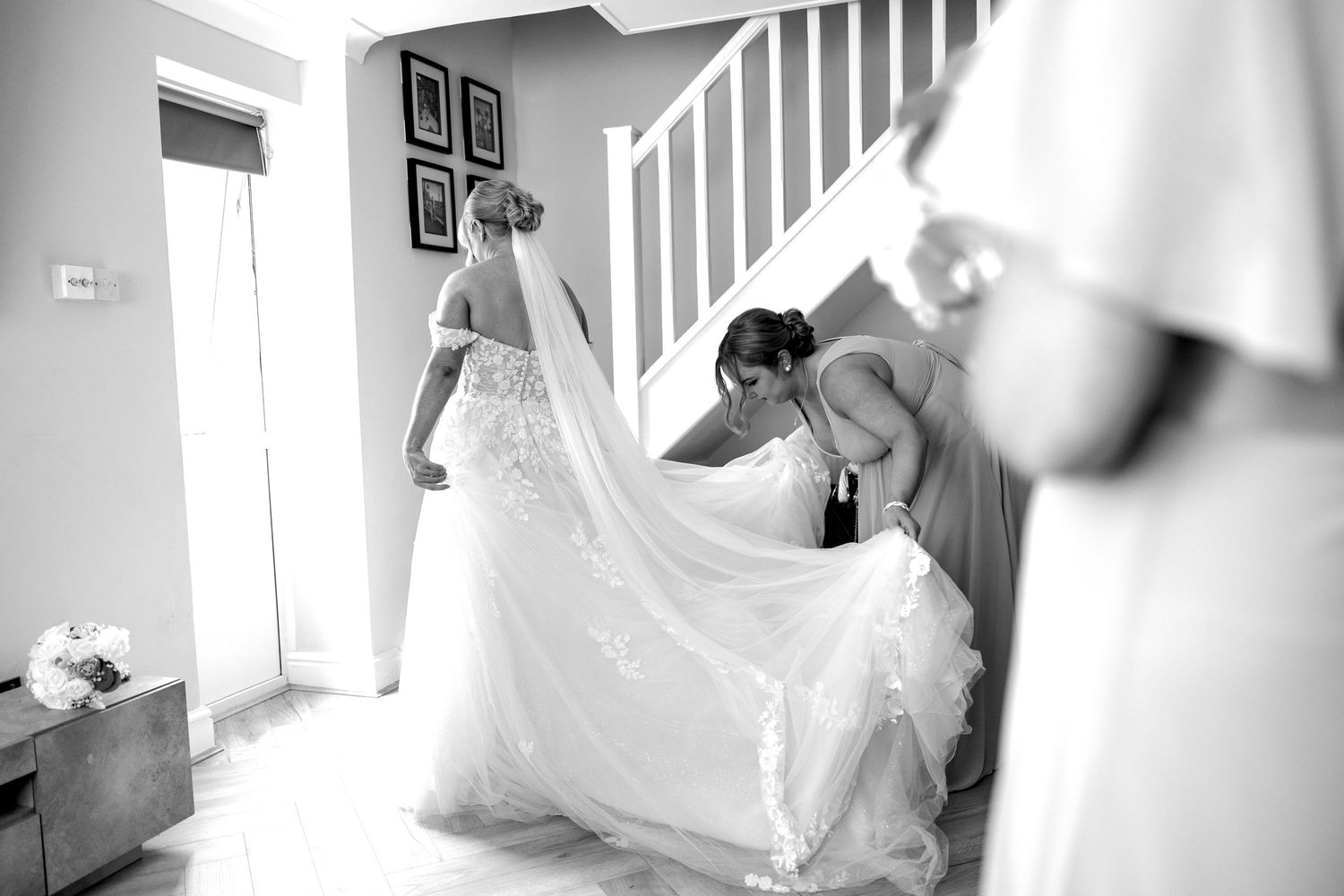 Black and white photo of bridesmaids helping the bride with her flowing wedding dress and veil on the stairs.