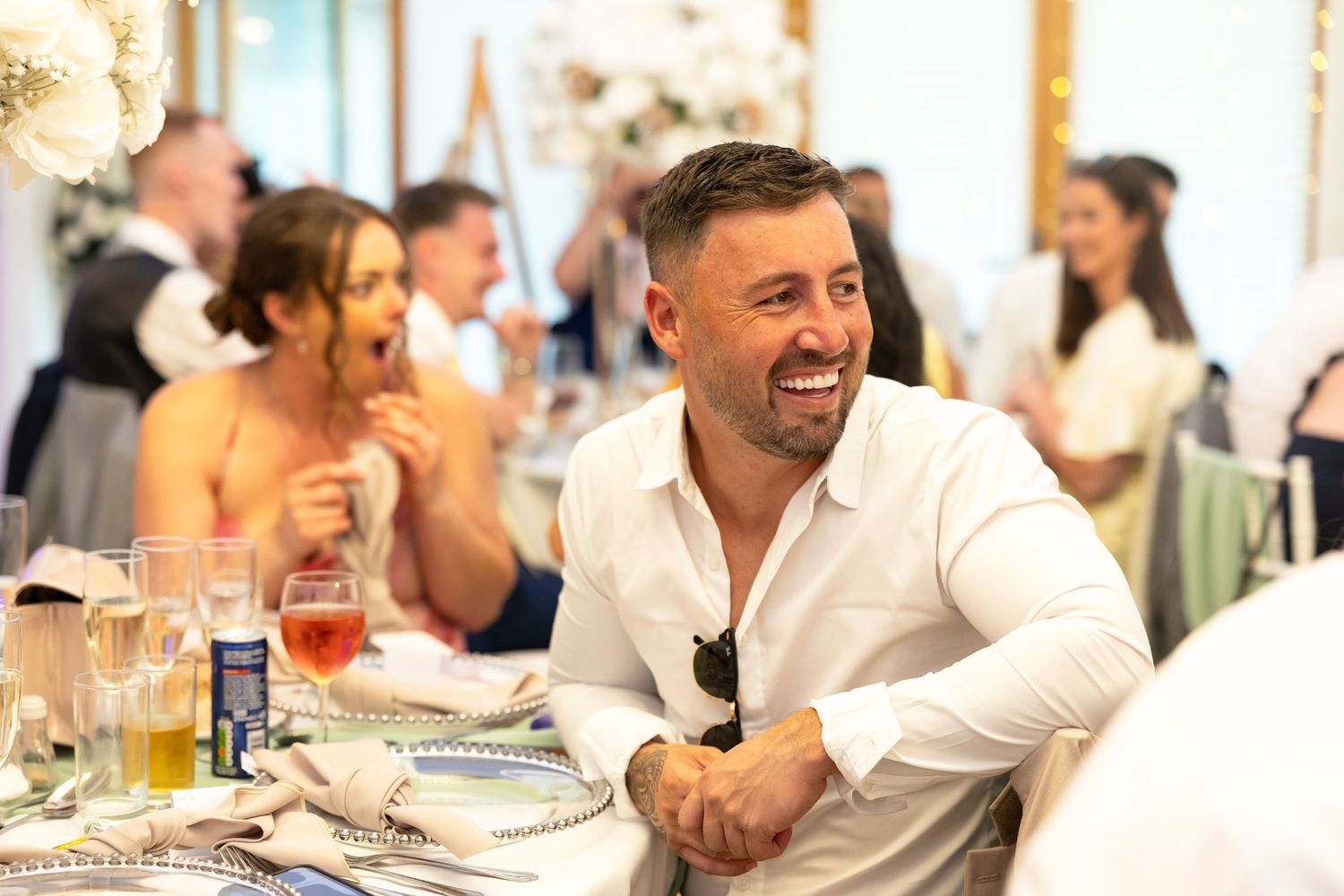 Man in white shirt laughing joyfully at a lively wedding reception.
