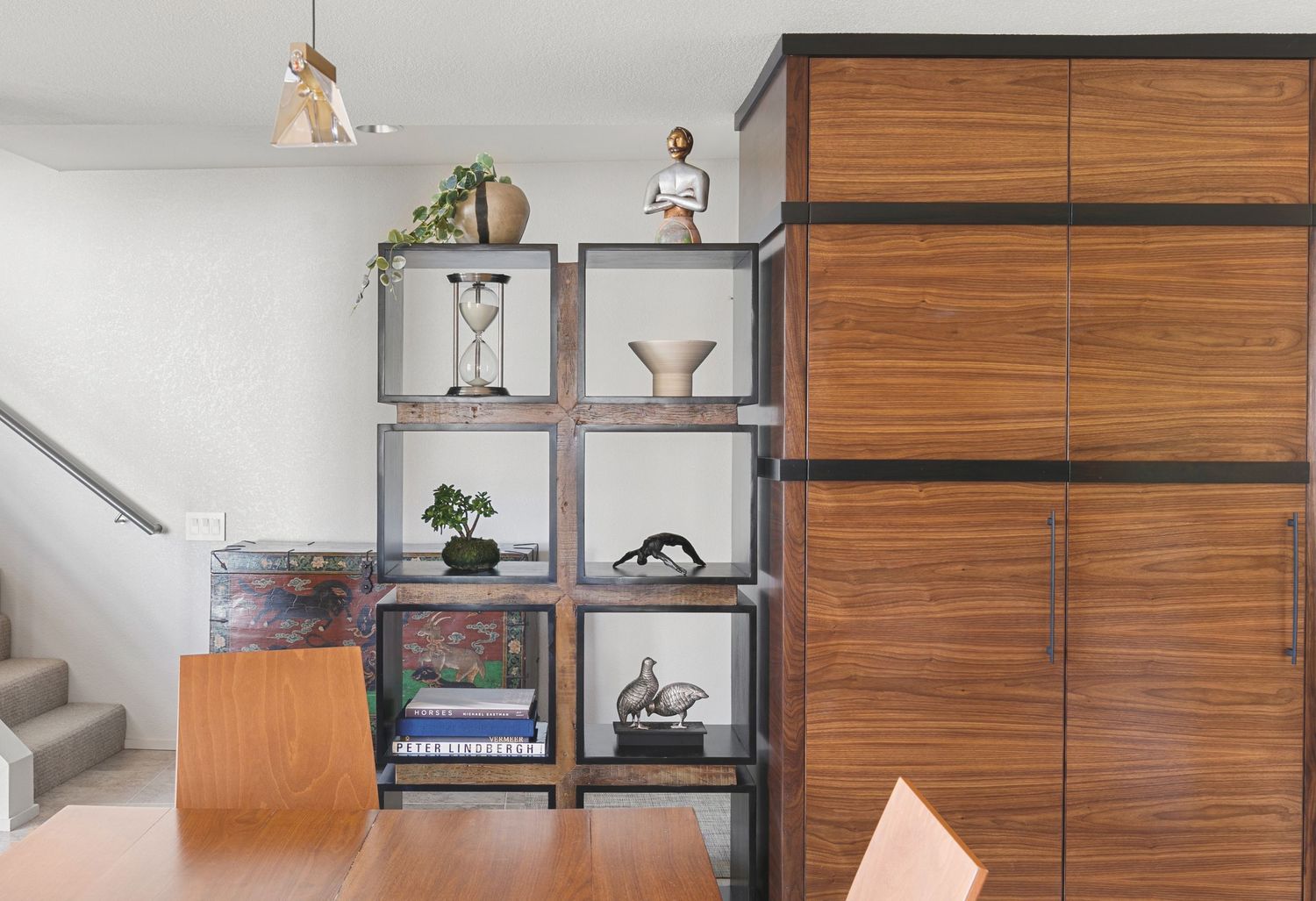 Modern living room with wood shelving unit displaying decor, books, and plants beside a large walnut cabinet.