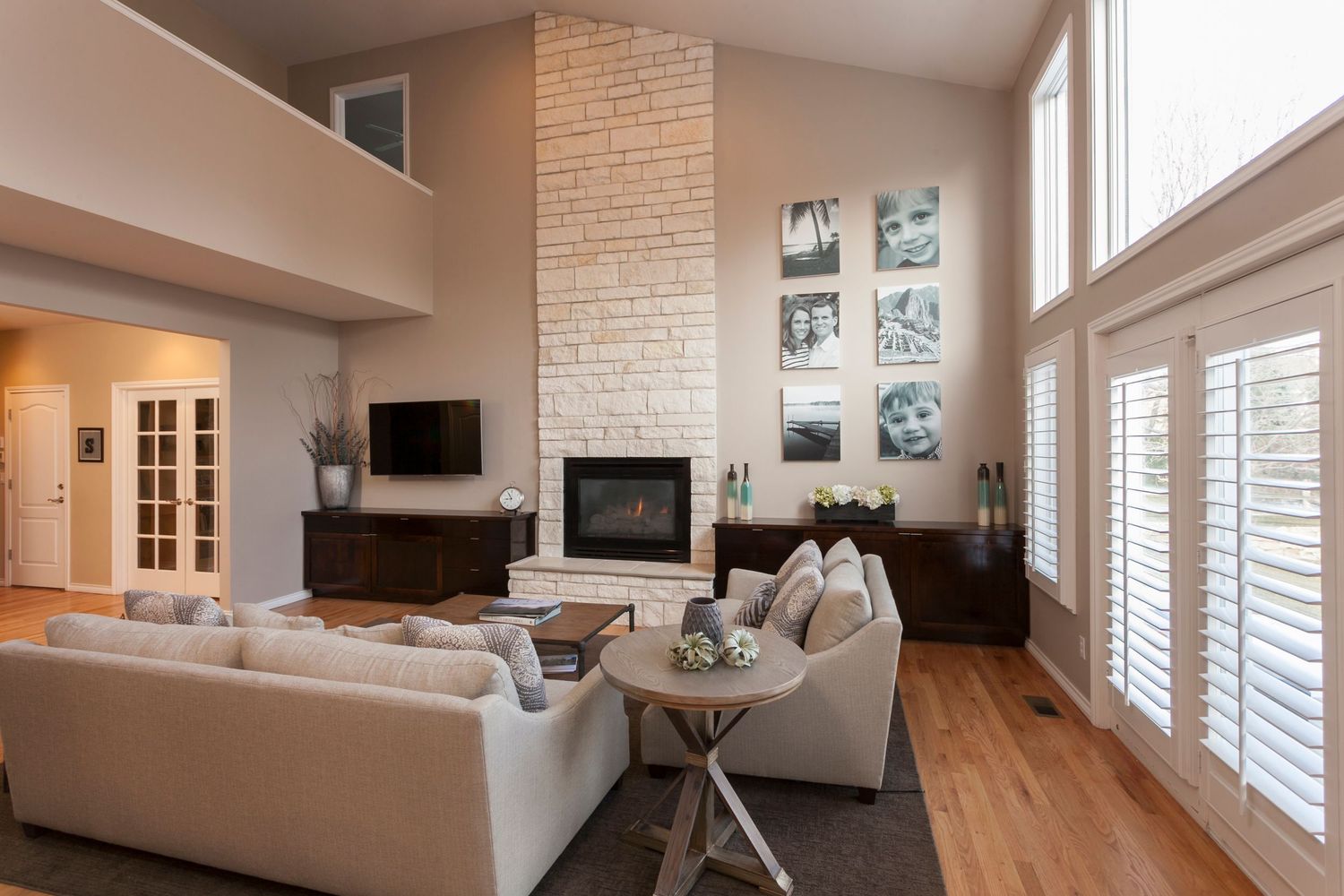 Modern living room with white brick fireplace, hardwood floors, neutral sofas, and large windows with plantation shutters.
