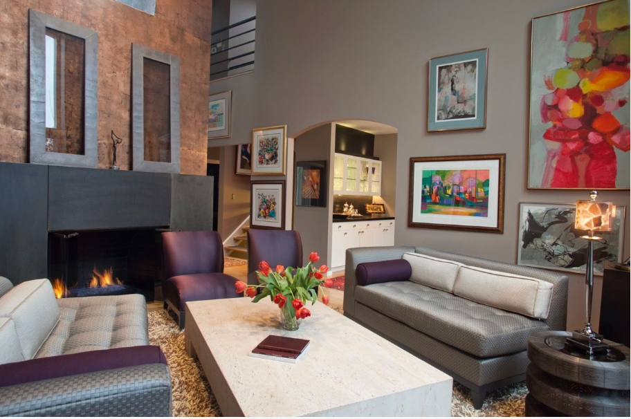 Modern living room with gray sofa, fireplace, colorful artwork, and high ceilings in an elegant loft space.
