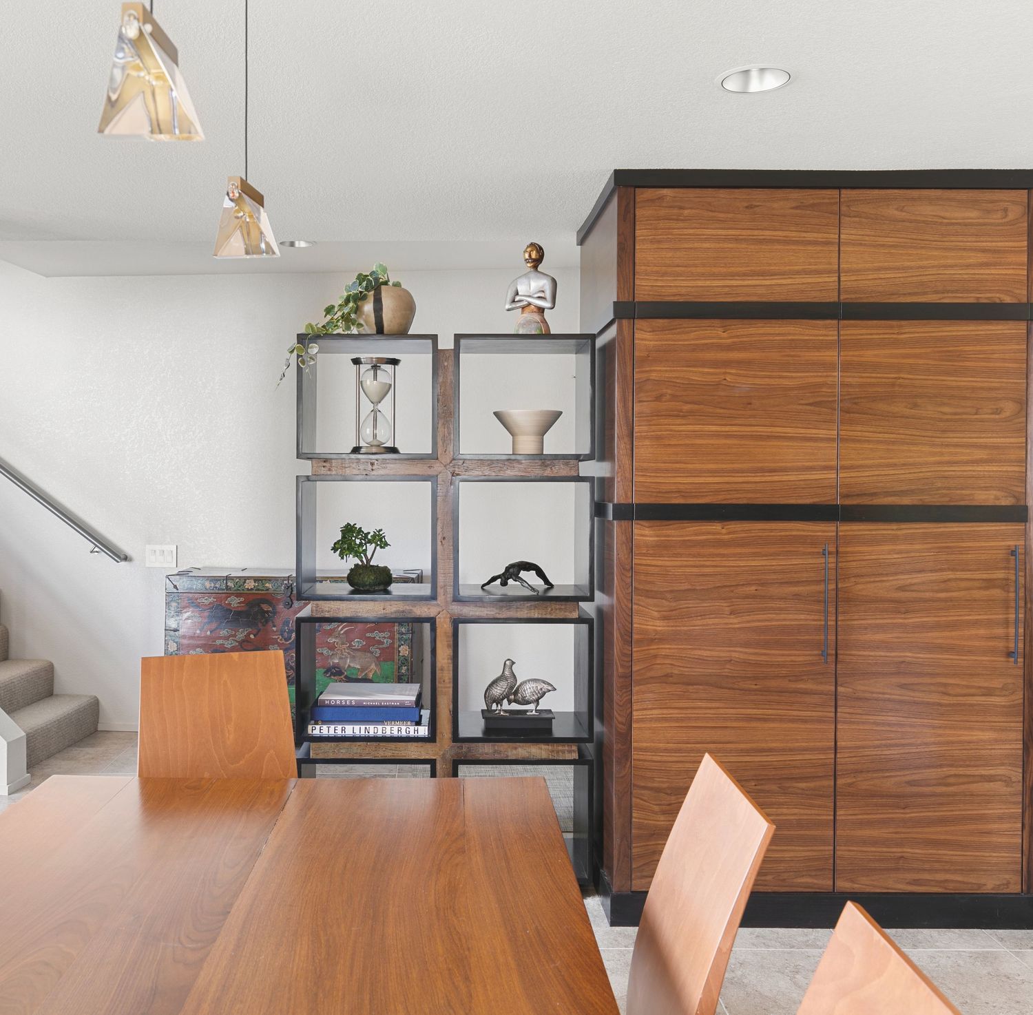 Modern dining room with wood table, chairs, open shelving unit displaying decor, and large walnut wood cabinet.