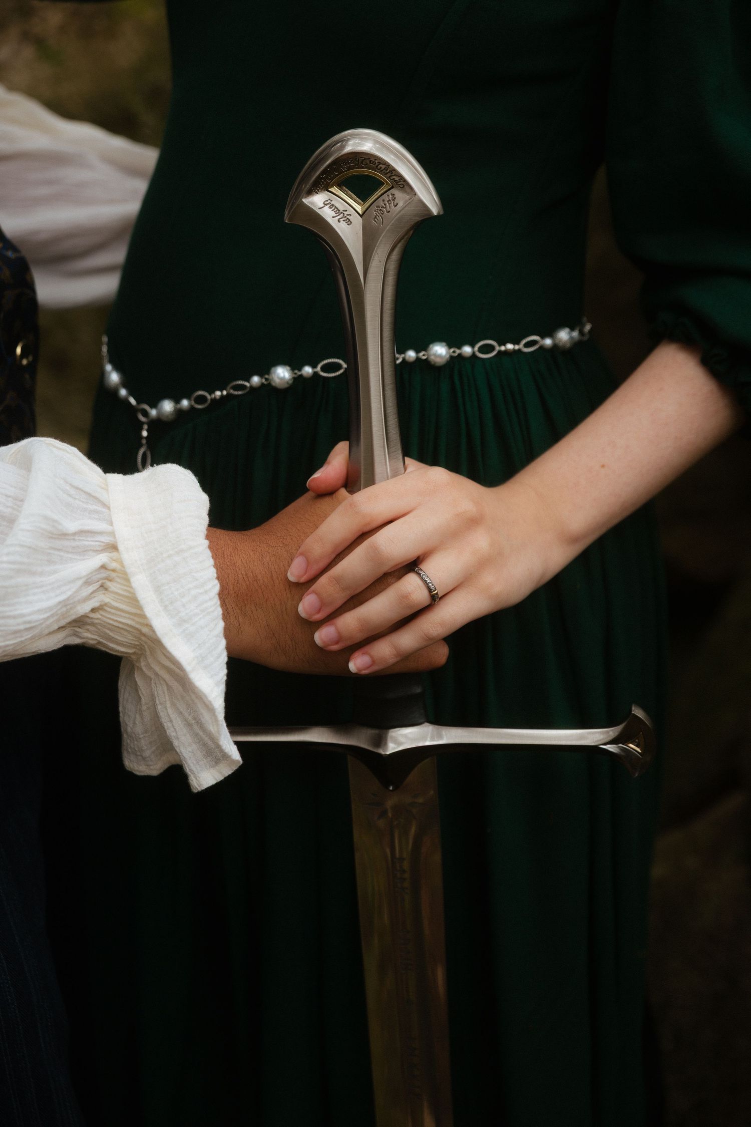Mãos de noivos seguram uma espada medieval, com roupas medievais fantasia, numa sessão fotográfica no dia do casamento em Sintra.