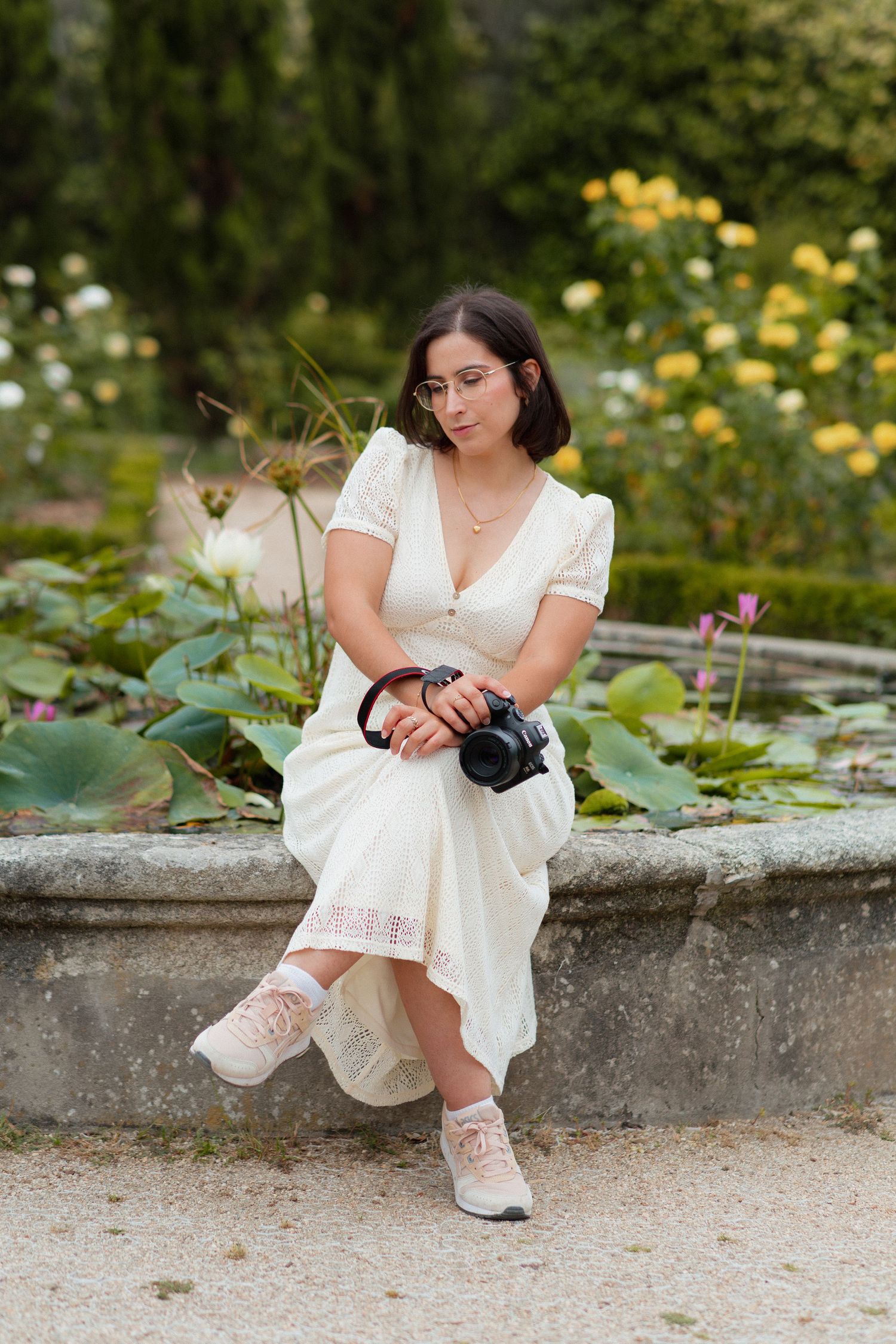 Cristiana Ribeiro sentada na beira de uma fonte, com água, vegetação e flores, a segurar câmara na mão, no Jardim Botânico do Porto.