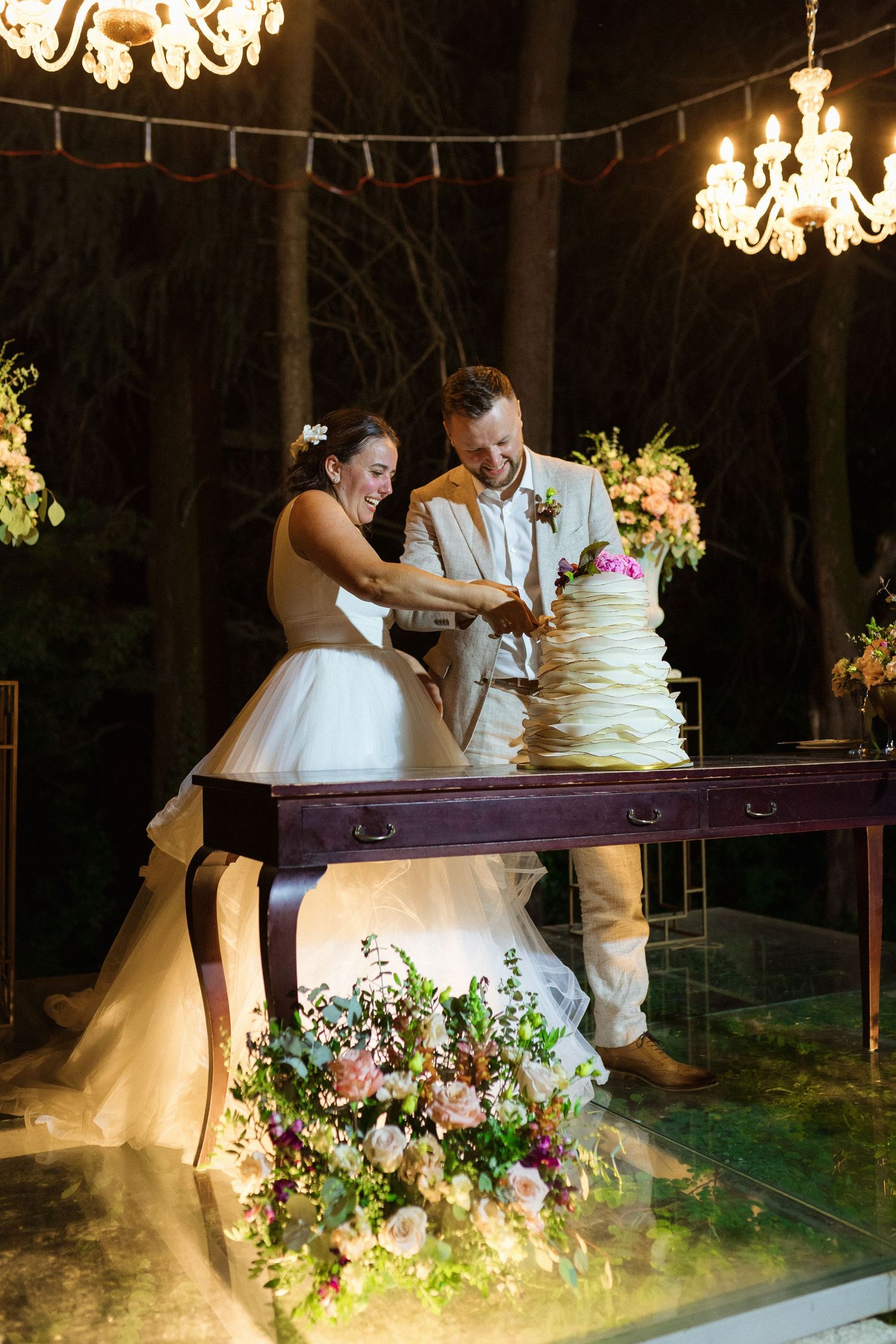Noivos durante o corte do bolo, junto a uma mesa decorada com flores e luzes quentes à volta, durante o casamento em Freamunde.