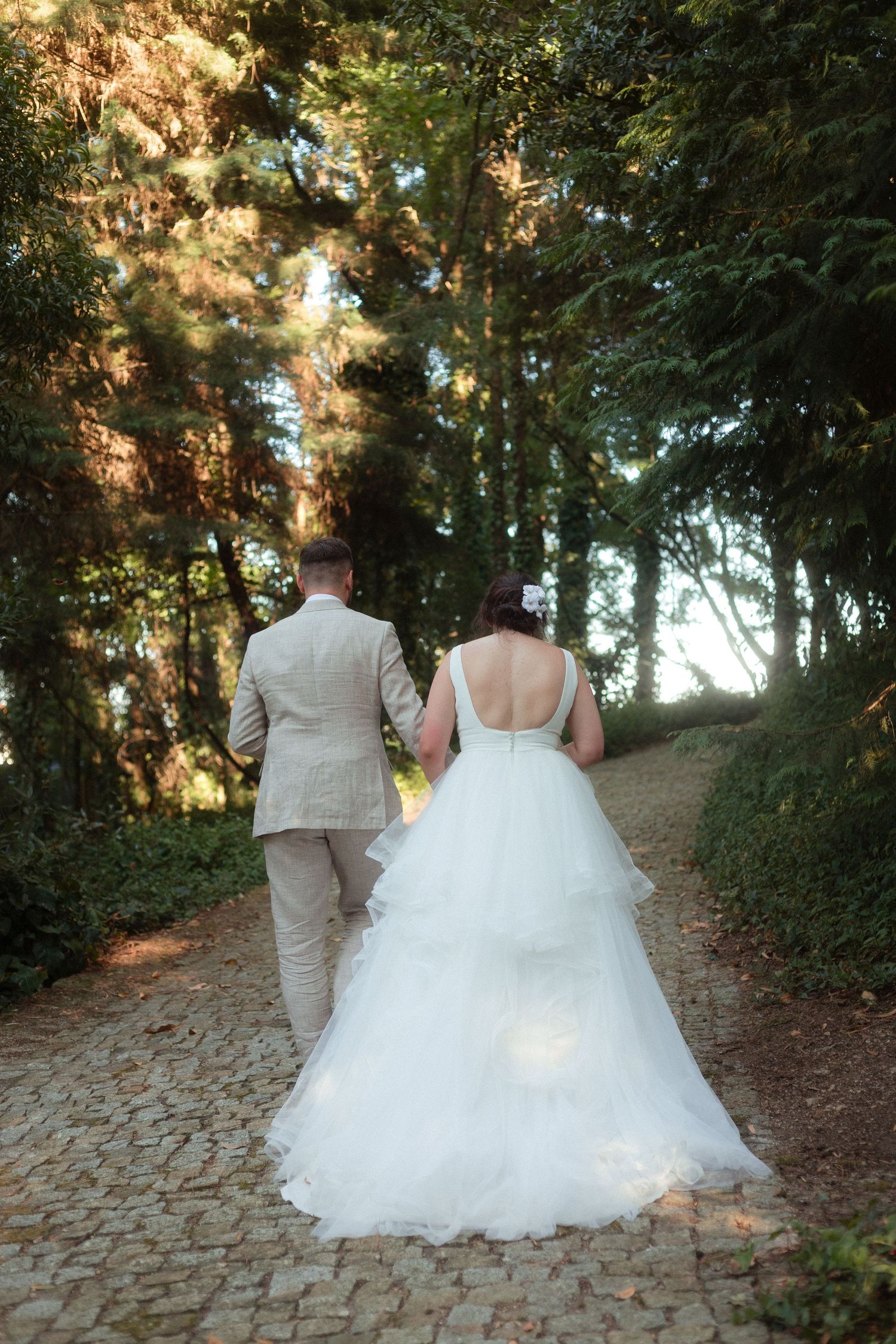 Noivos caminham de costas, de mãos dadas, ao final da tarde, no meio de floresta, no dia do casamento em quinta em Freamunde.