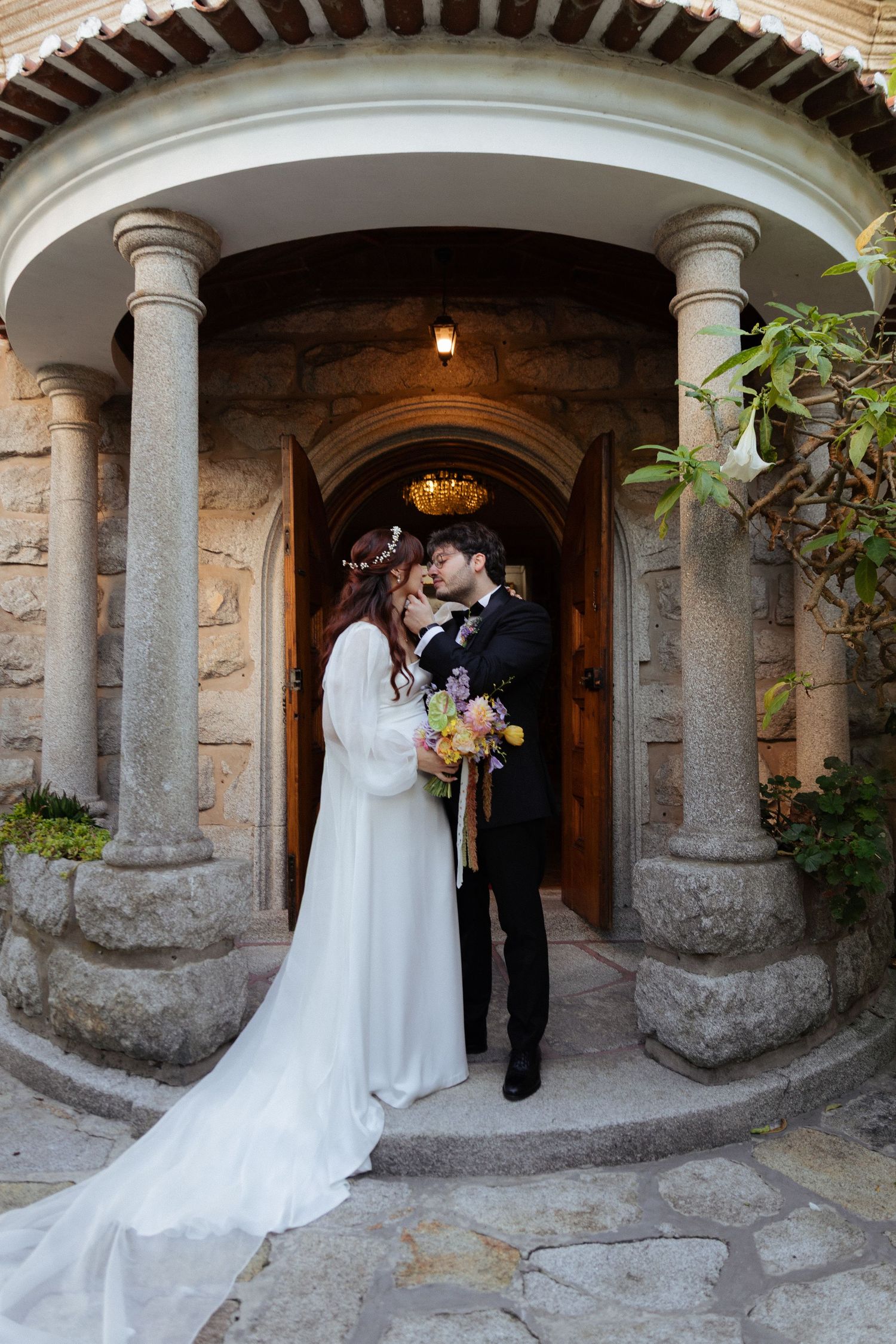 Noivos abraçam-se em entre arcos de pedra antigos, rodeados por vegetação e arquitetura histórica, em casamento no Porto.