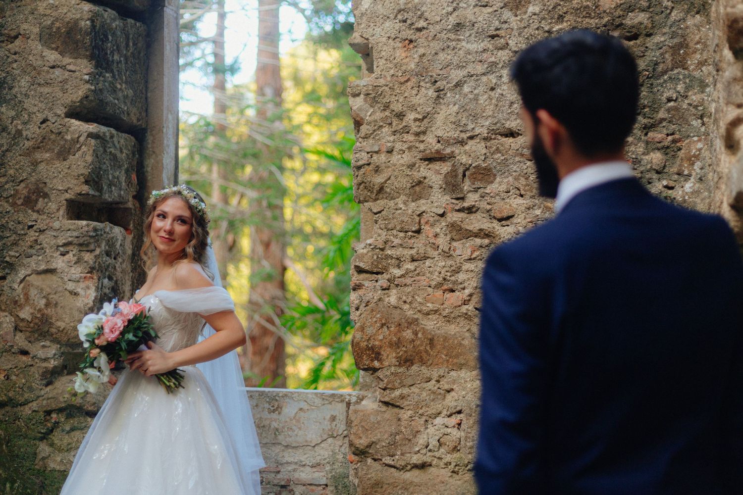 Noiva segura um bouquet enquanto olha para o noivo e sorri, numa sessão de trash the dress nas ruínas de uma capela, em Monserrate, Sintra.