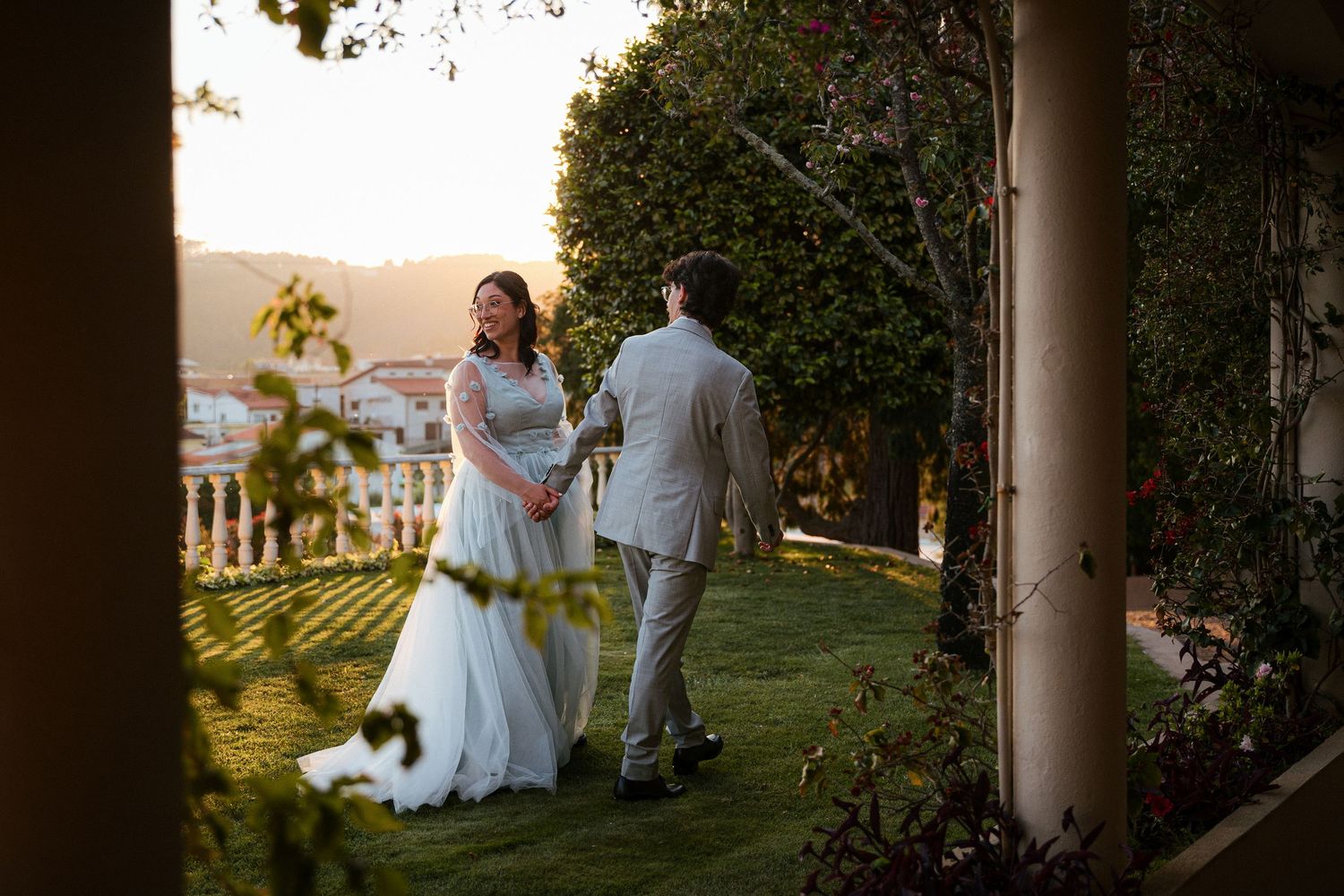 Noivos caminham junto a uma casa histórica, rodeados por natureza e pôr do sol, durante o casamento, numa quinta em Santo Tirso.