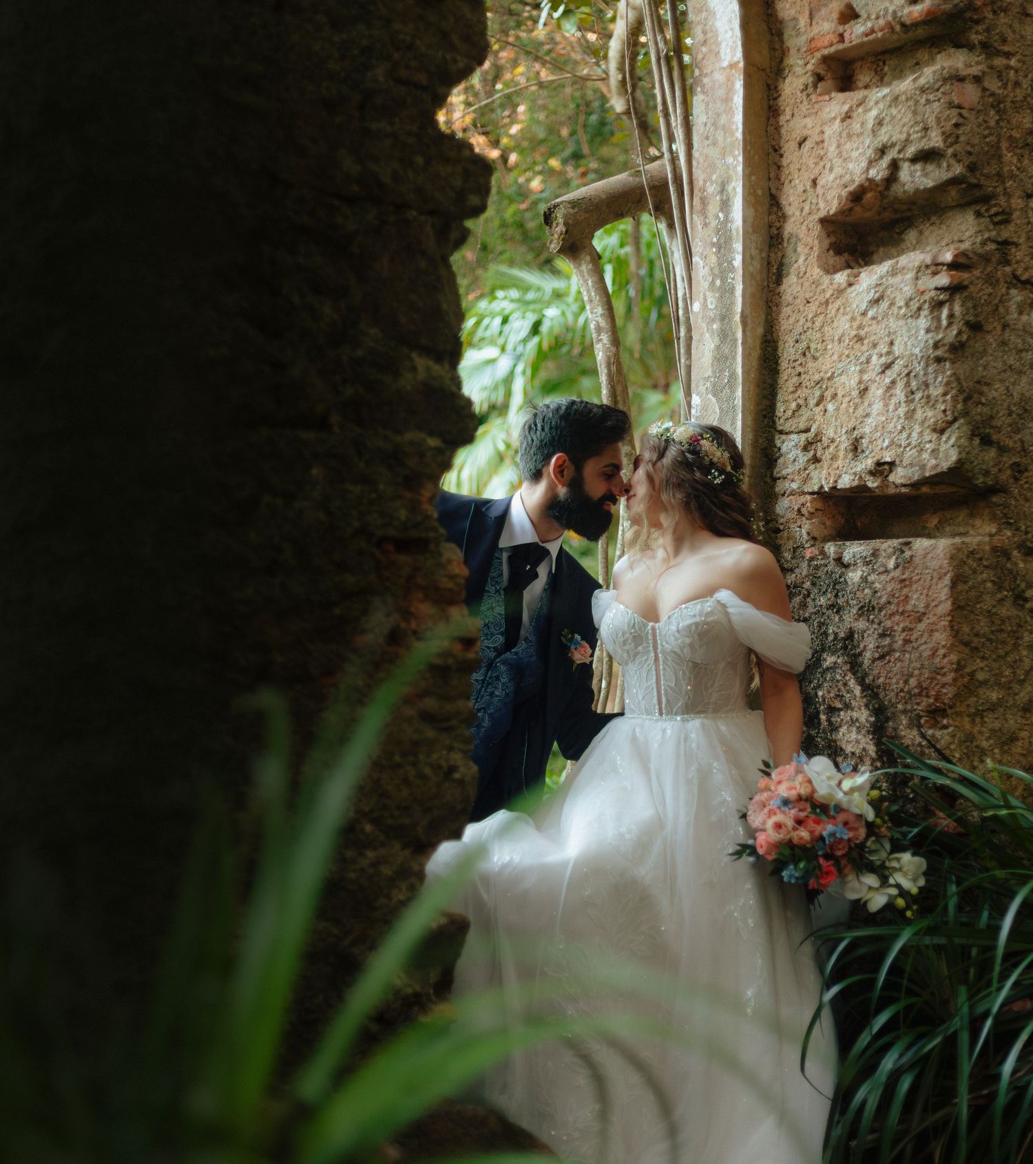 Noivos em quase beijo, numa janela de capela em ruínas rodeada por flores e vegetação, em Monserrate, Sintra.