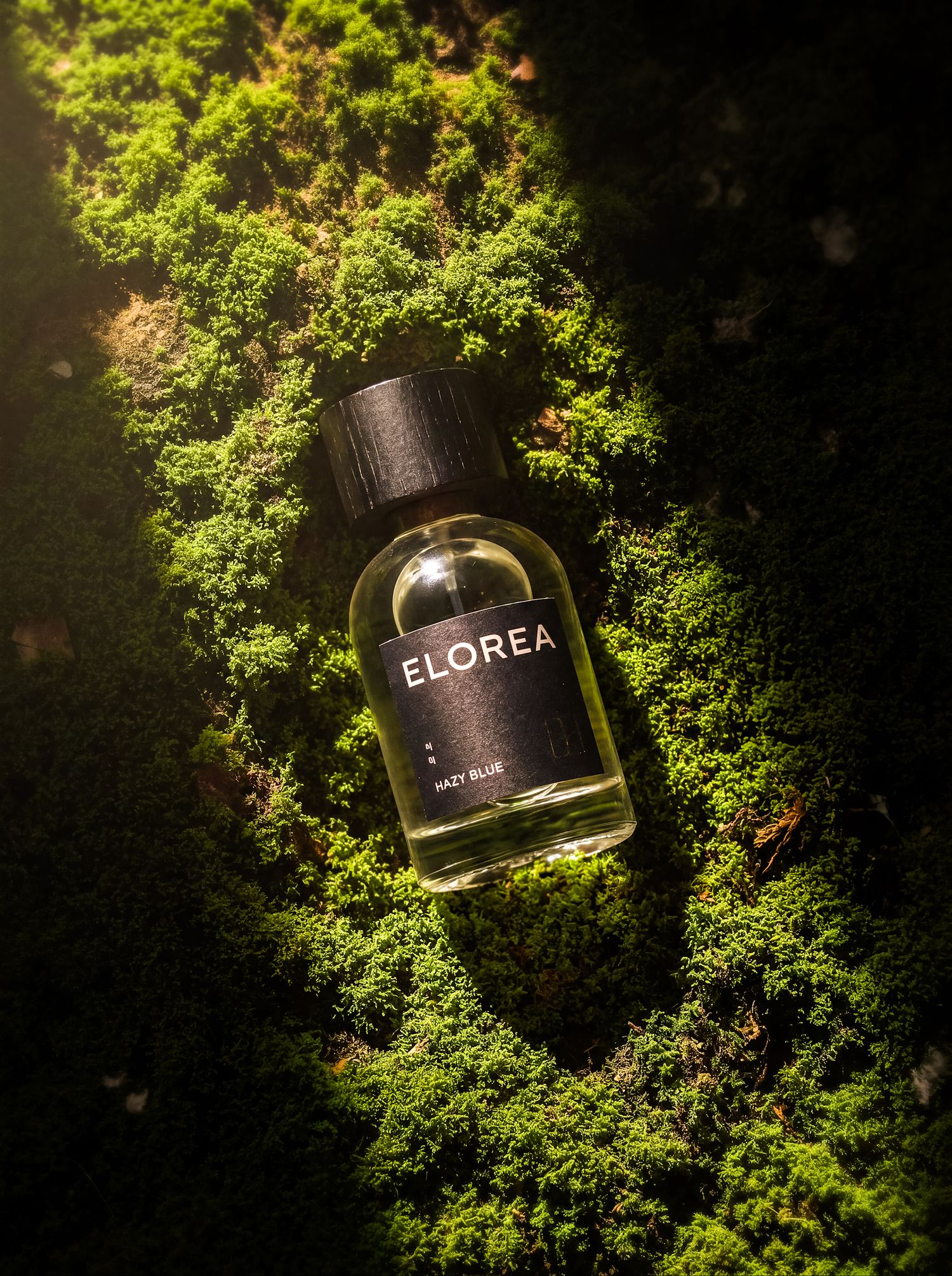 Dark fragrance bottle arranged on vivid green moss.