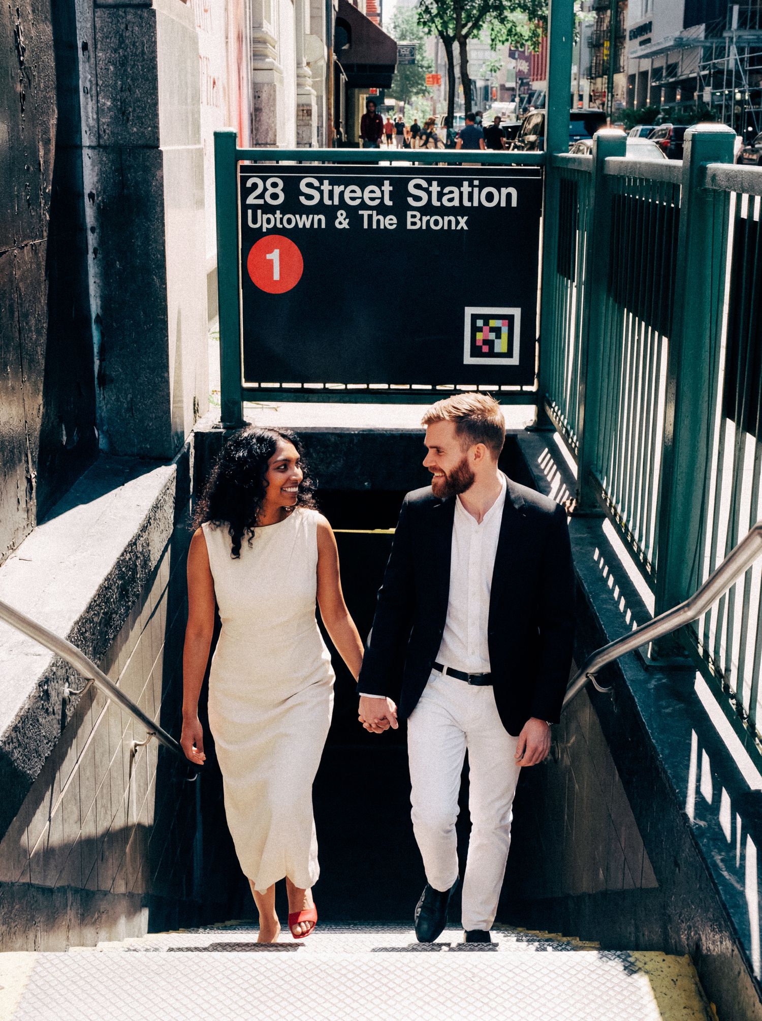 Newlyweds walking hand in hand into a New York City subway station.