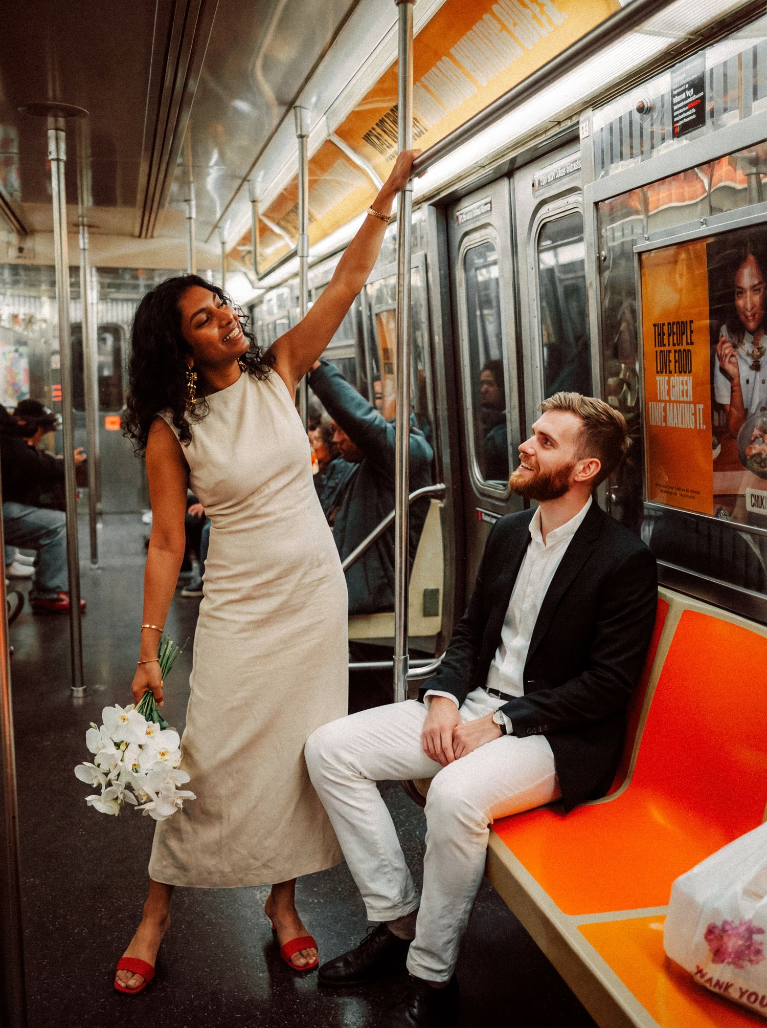 Bride standing beside her seated groom inside a New York subway car.