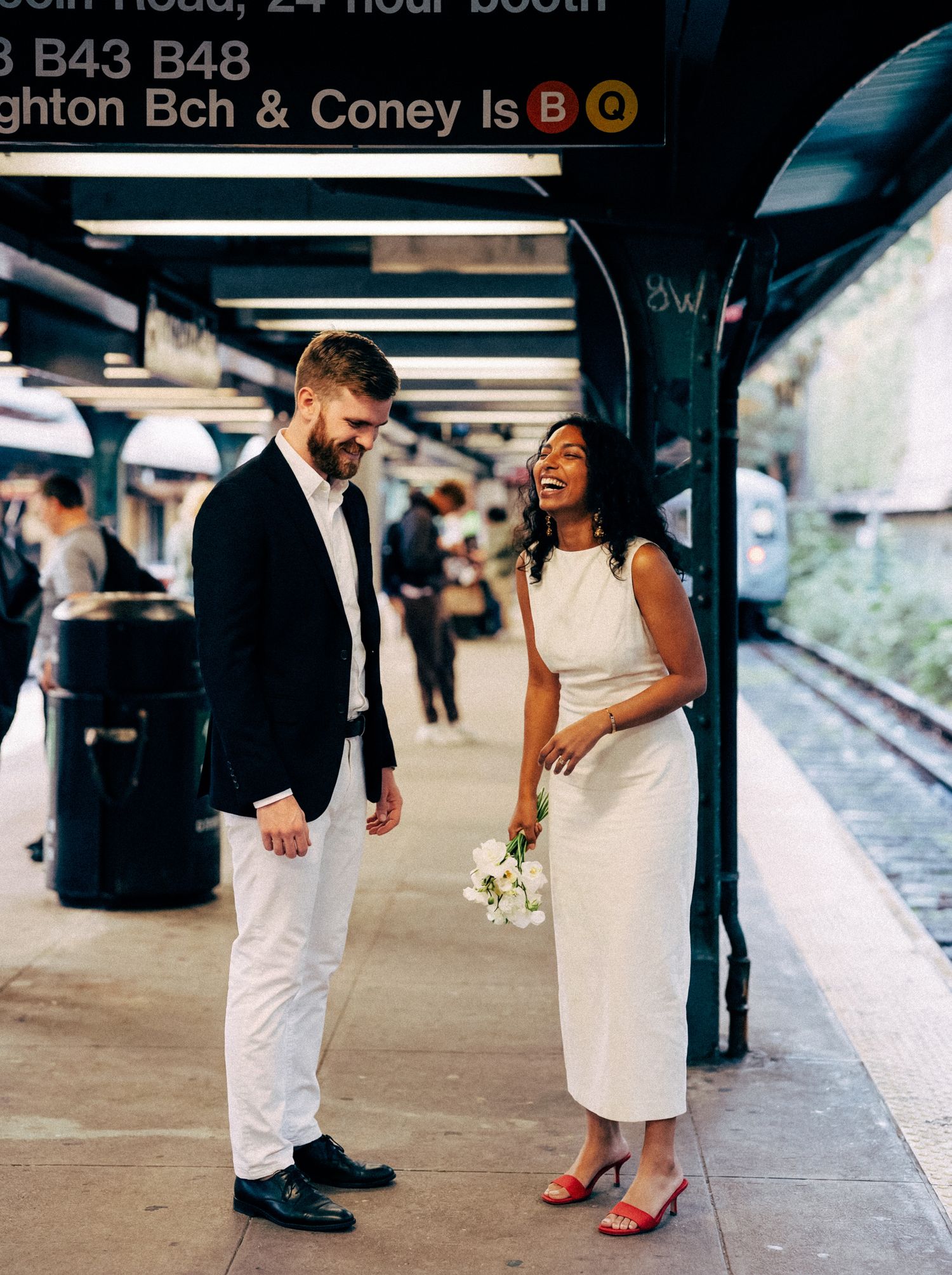 Newlywed couple sharing a candid moment on a New York subway platform.